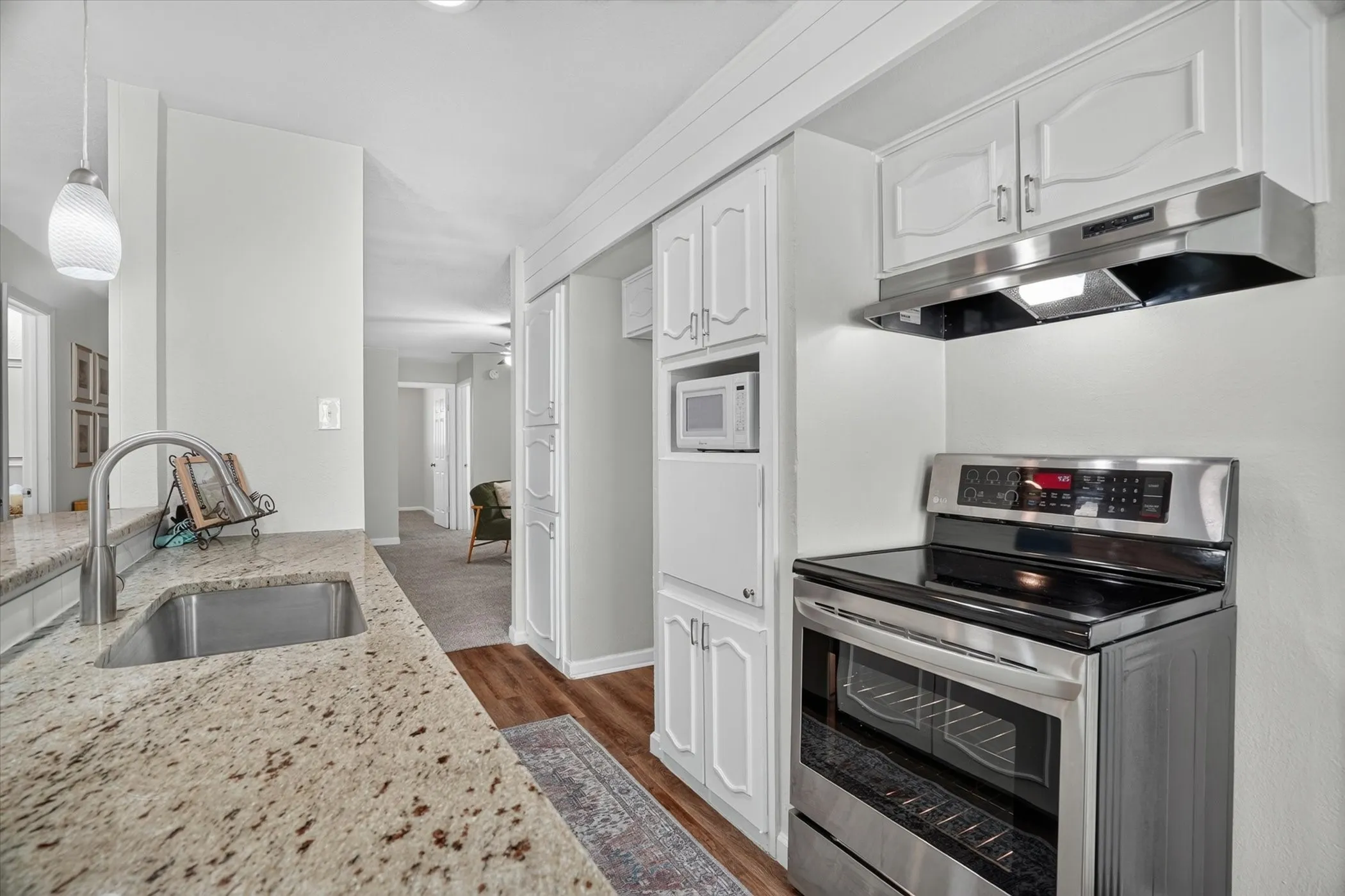 Kitchen featuring granite countertops, stainless steel sink with gooseneck faucet, white cabinetry, wood-finish flooring, and a stainless steel range with overhead ventilation