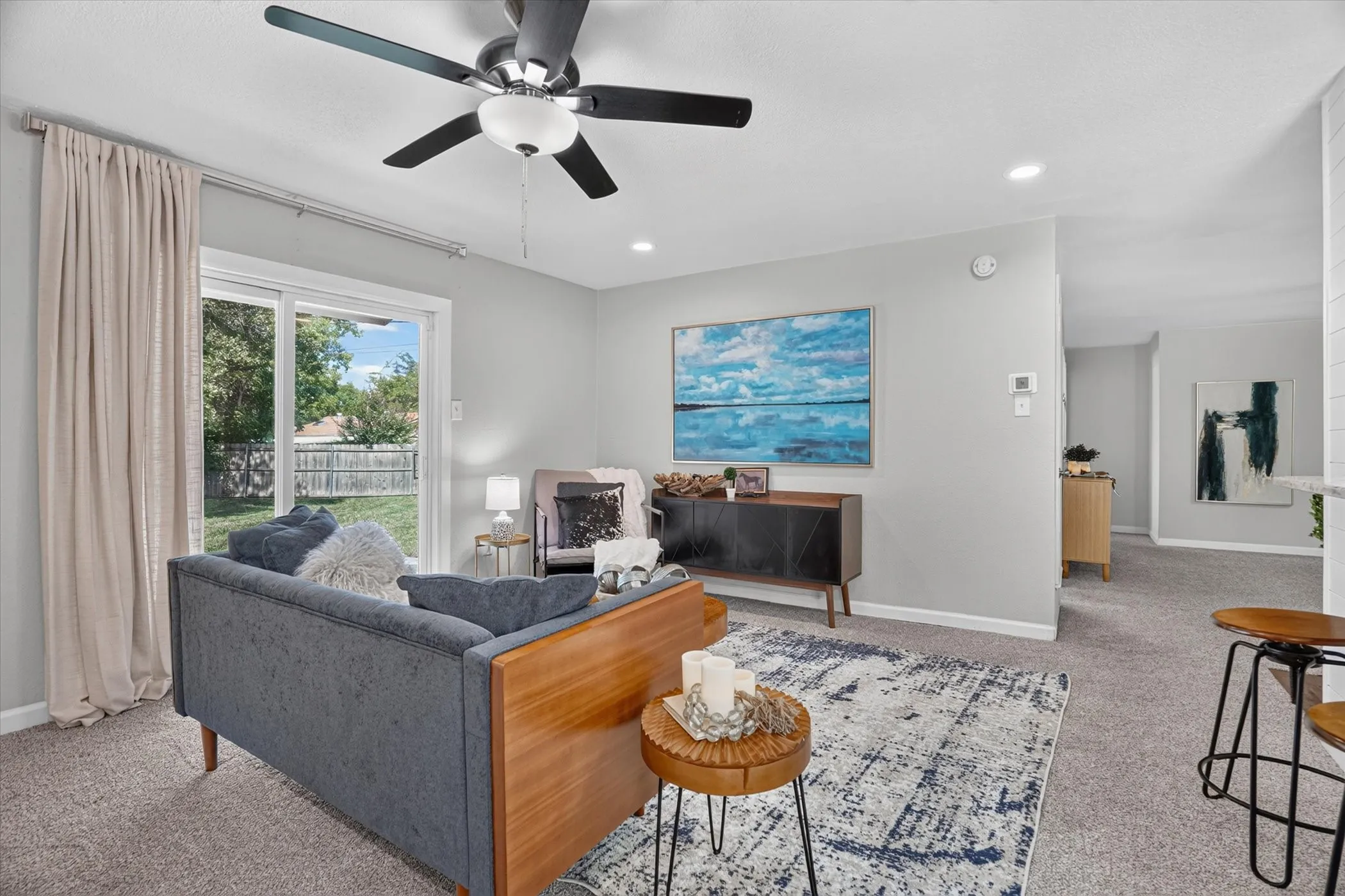 Spacious living area featuring light gray walls, plush gray carpeting, and a ceiling fan with integrated lighting
