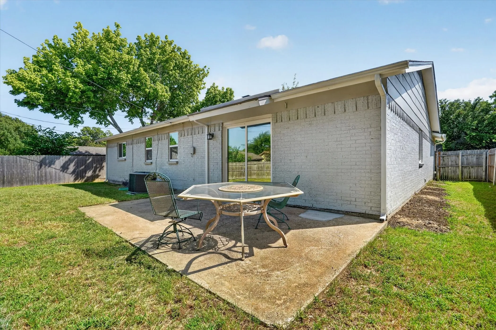 Rear exterior featuring a concrete patio, sliding glass door, and light-painted brick siding
