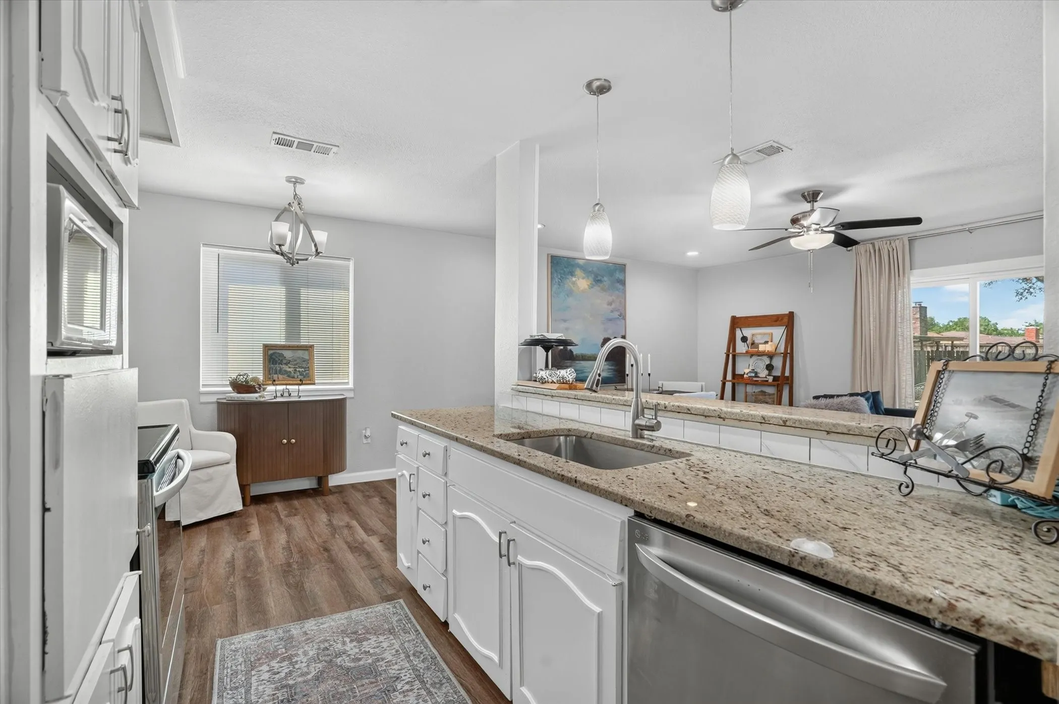 Kitchen featuring an island with a stainless steel sink, granite countertops, white cabinetry, and wood-finish flooring