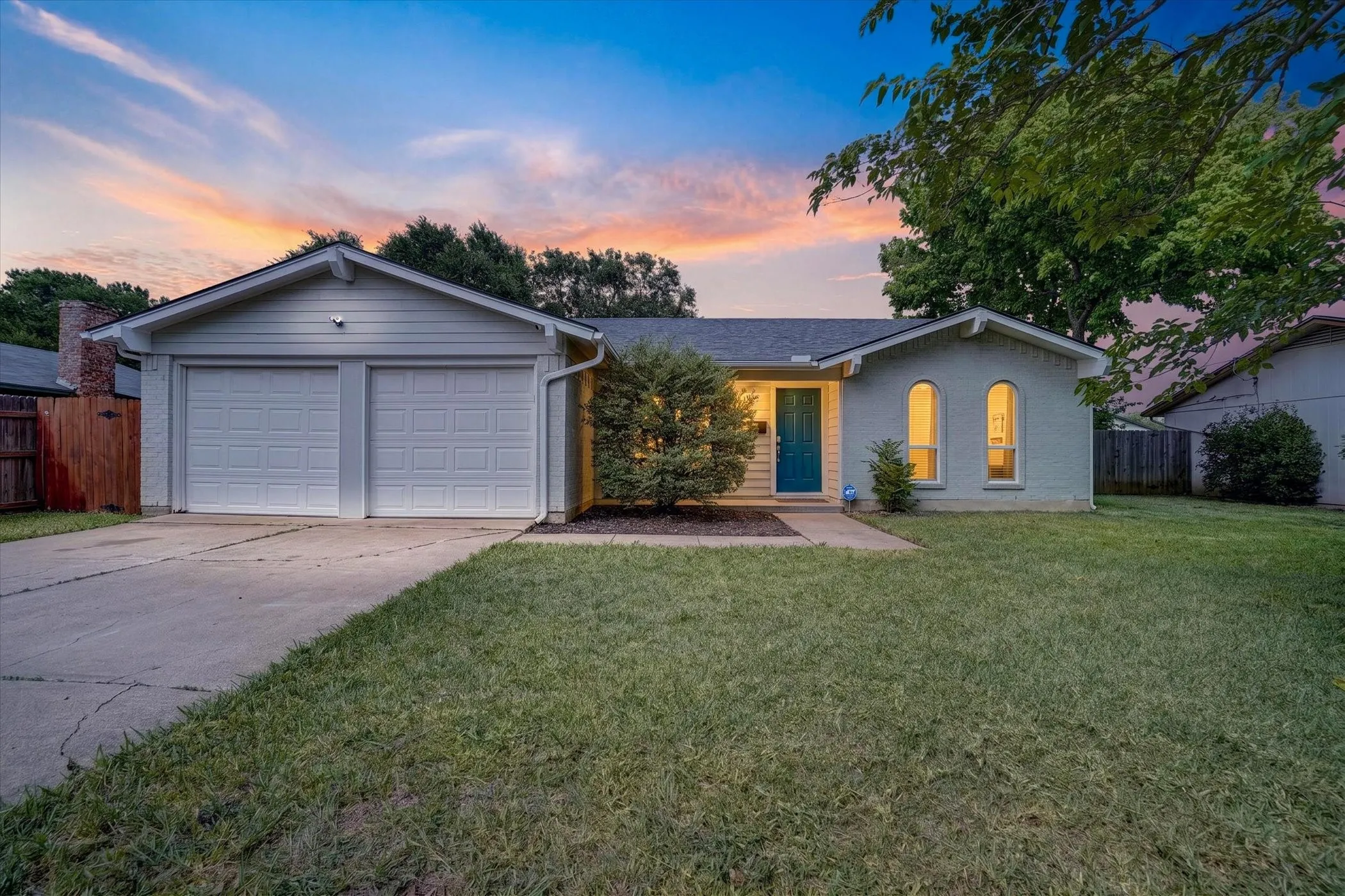 Single-story residence featuring a two-car garage, light-colored exterior siding, a distinct teal front door, and arched window accents