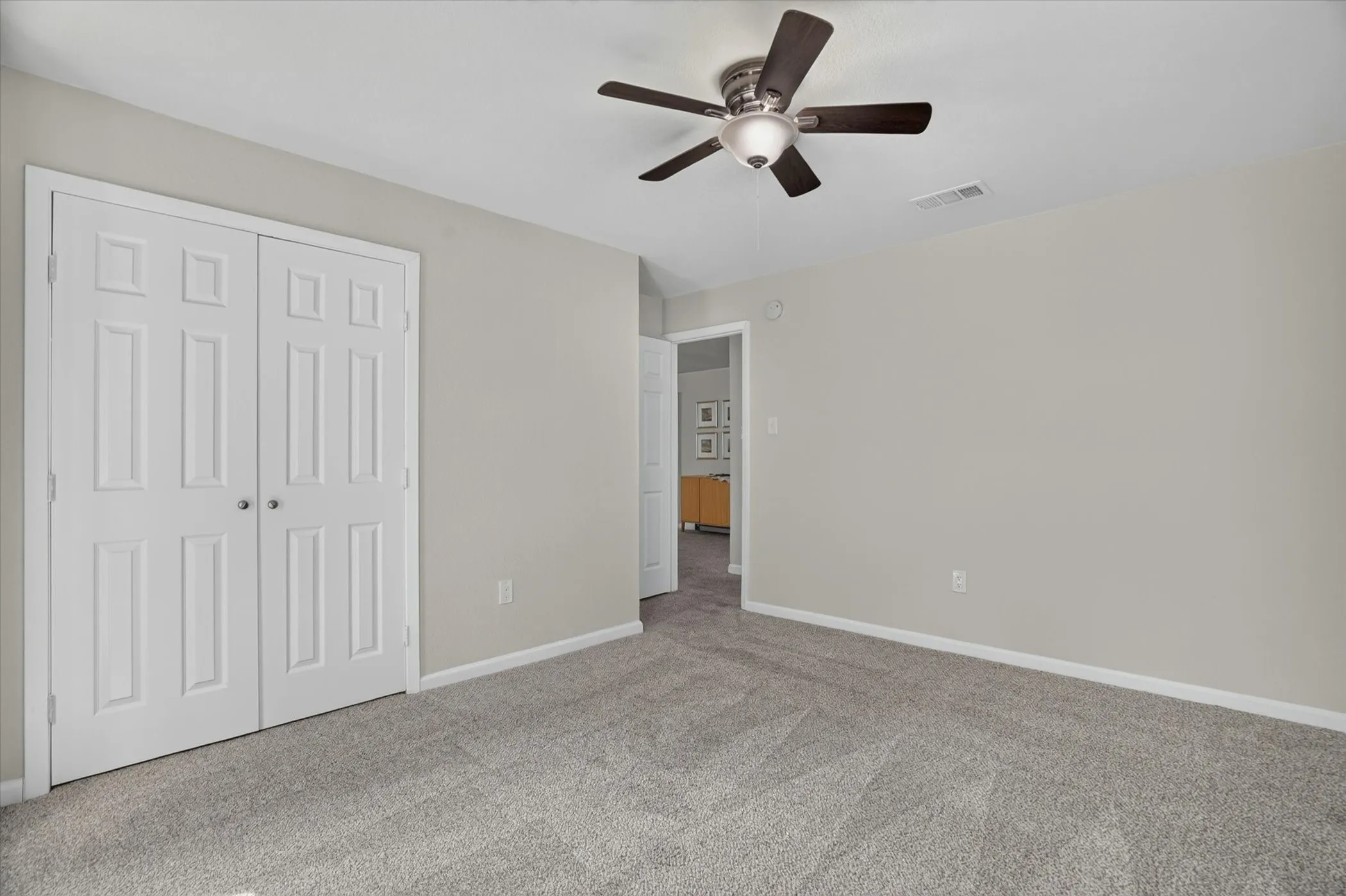 Neutral gray wall paint with white trim, gray carpet flooring, and a dark-toned ceiling fan with integrated lighting