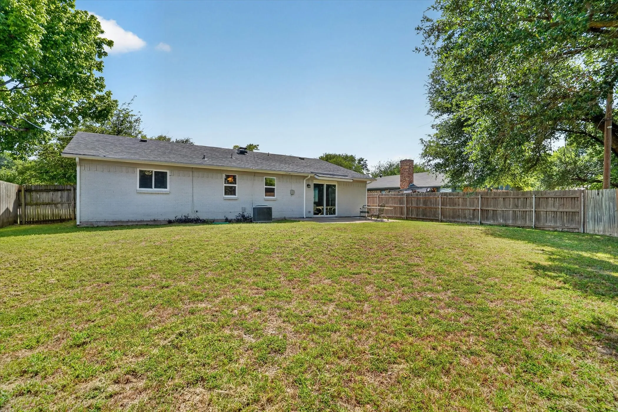 Expansive fenced backyard featuring a substantial lawn area, a back patio, and mature perimeter trees