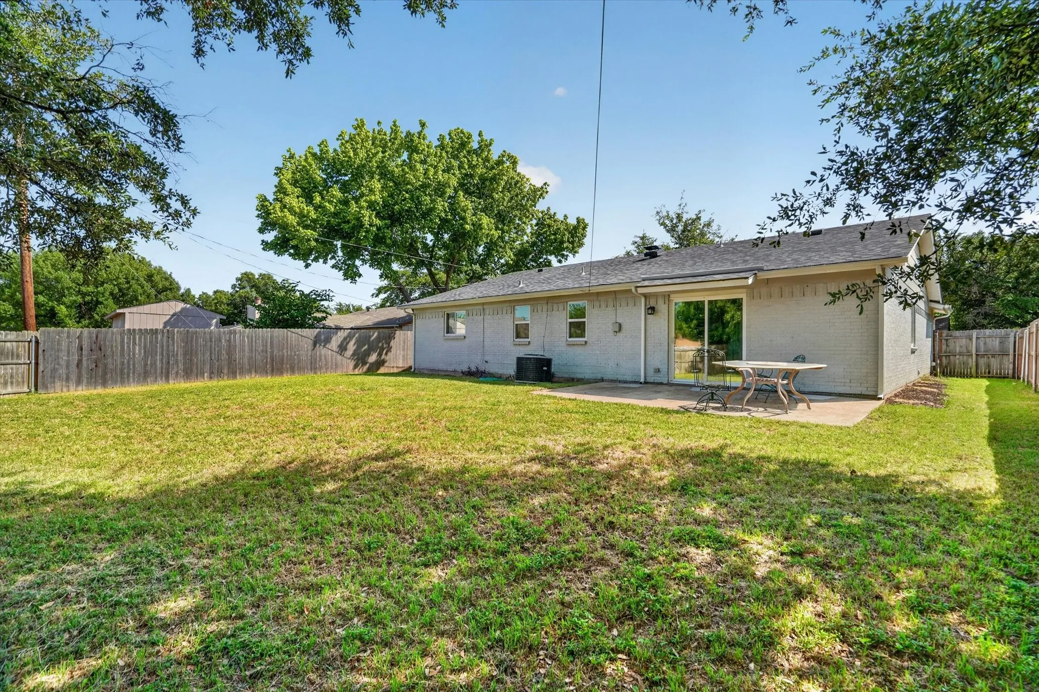 Expansive backyard featuring a manicured lawn, full privacy fencing, and a concrete patio