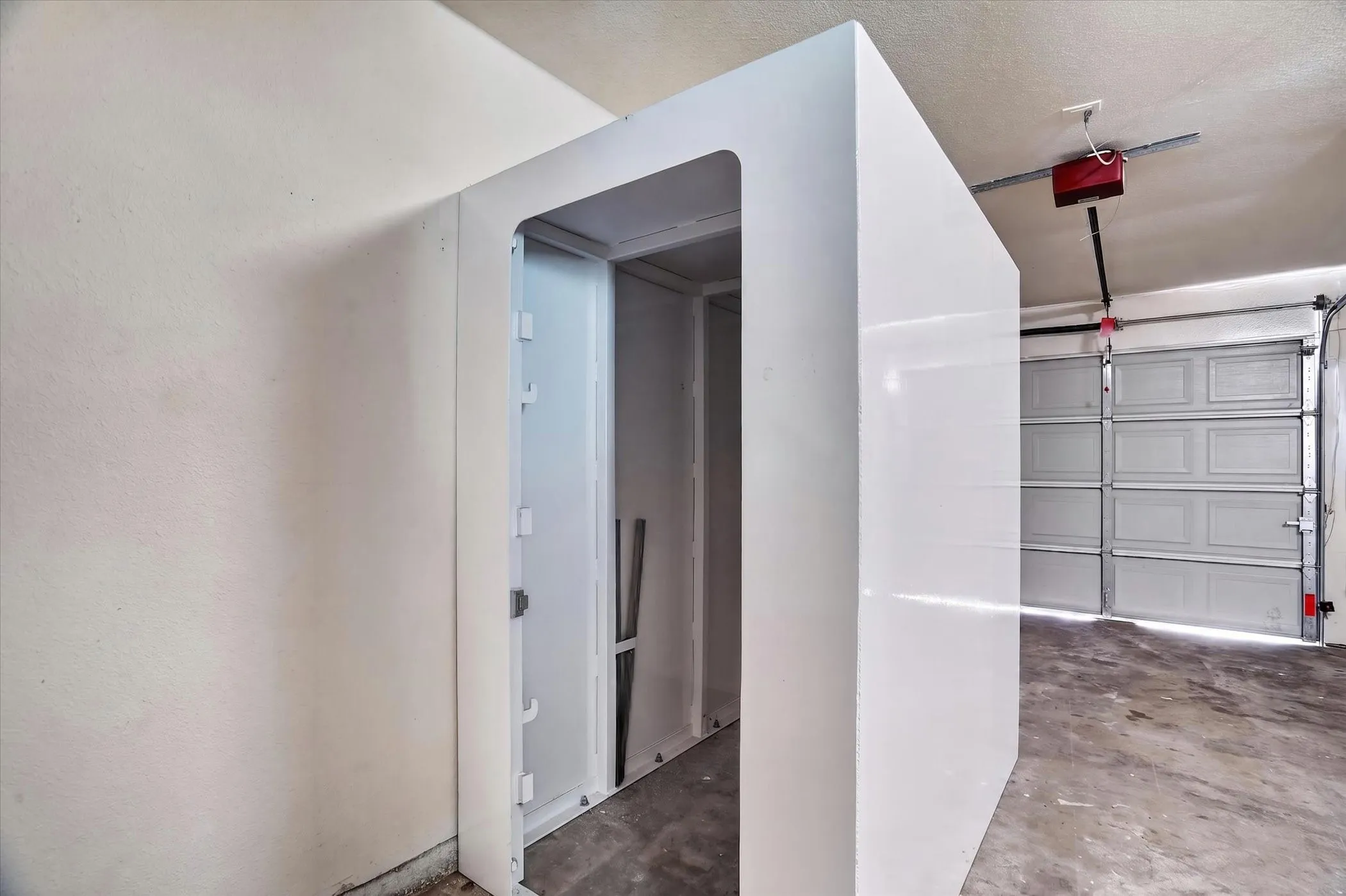 Integrated interior room within a garage space, featuring a durable concrete floor and an overhead garage door opener mechanism