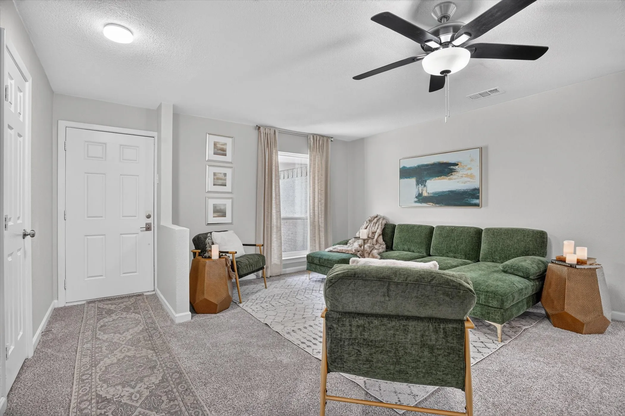 Living area featuring light gray wall paint, textured carpeting, a white paneled entry door, and a ceiling fan with integrated lighting