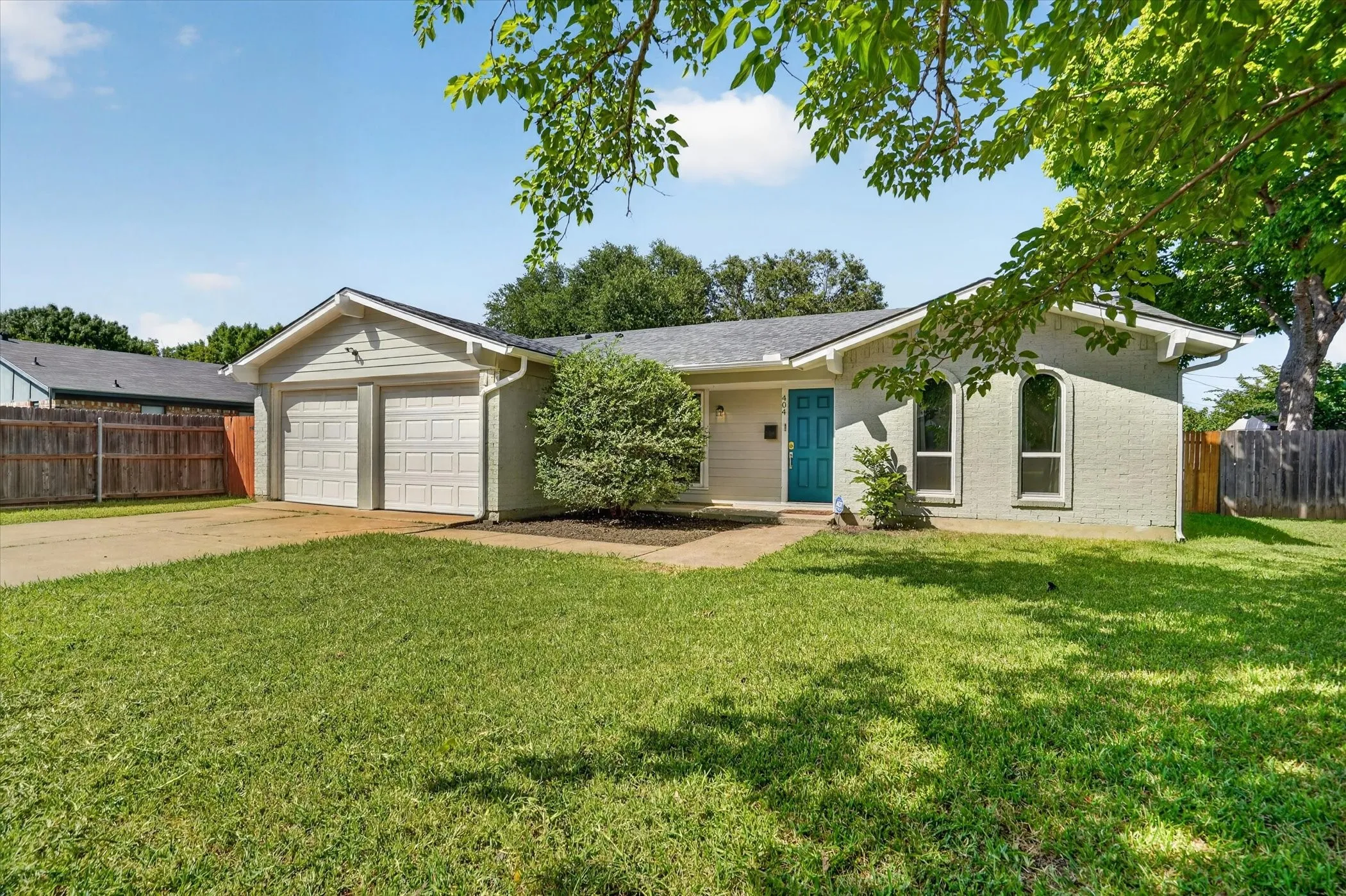 Front exterior featuring a two-car garage, a vibrant turquoise entry door, and arched window details
