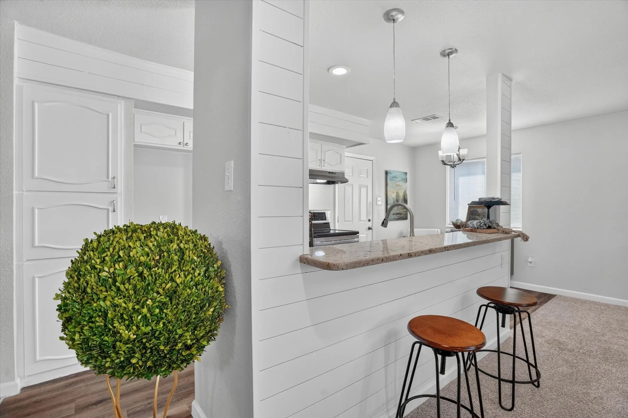 Kitchen bar featuring a stone countertop, shiplap-style paneling, and two pendant lights