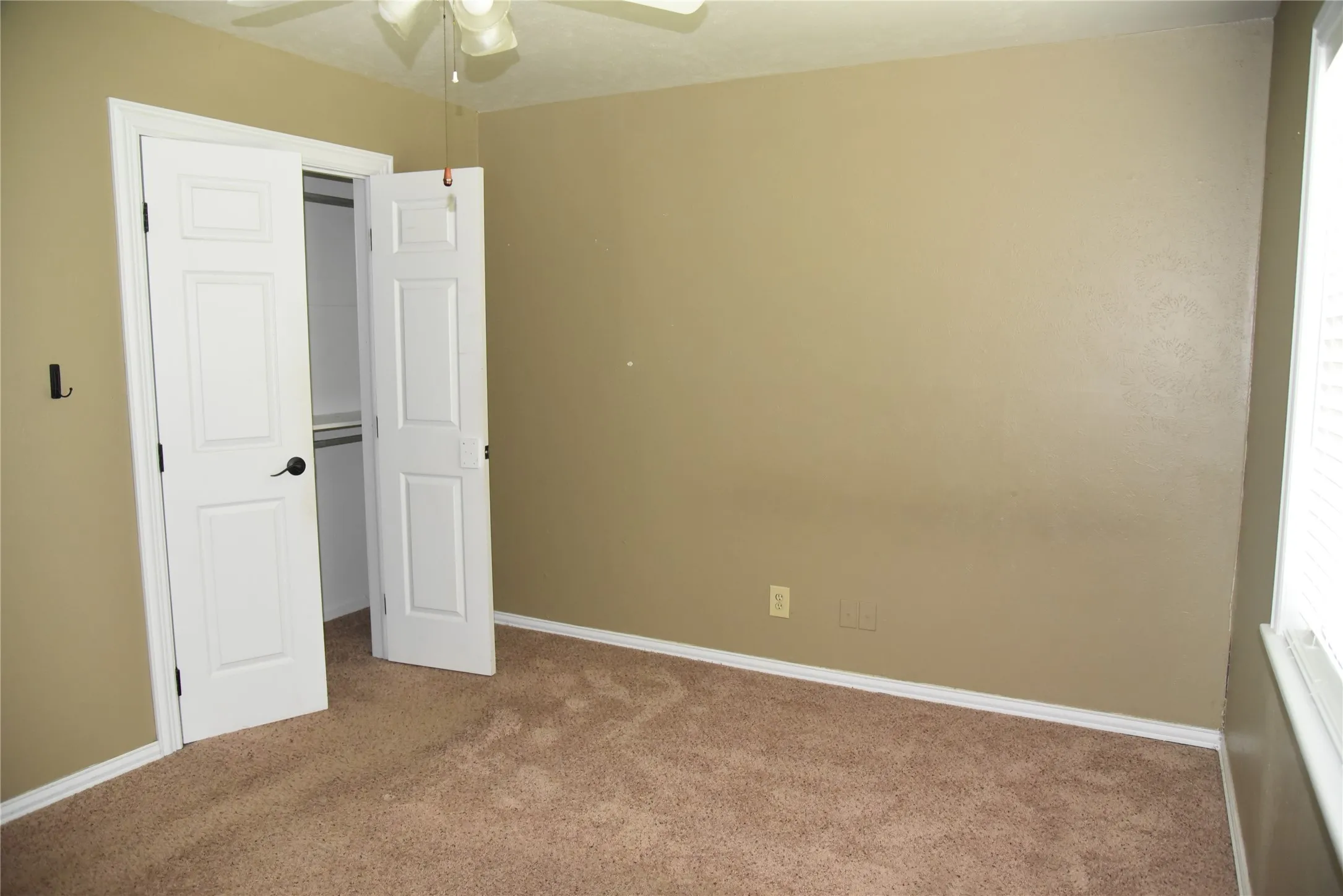 Carpeted room featuring a ceiling fan, a window with horizontal blinds, and a bi-fold closet with shelving and hanging rods