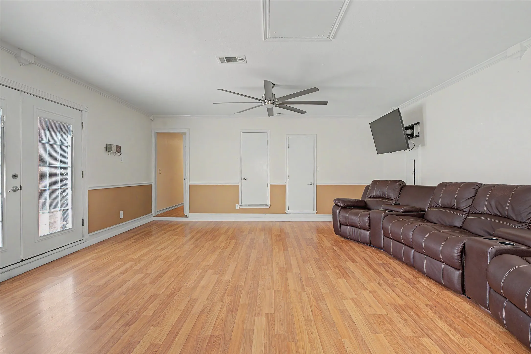 Spacious room featuring wood-finish flooring, white walls with a chair rail, a ceiling fan, and double doors with glass paneling