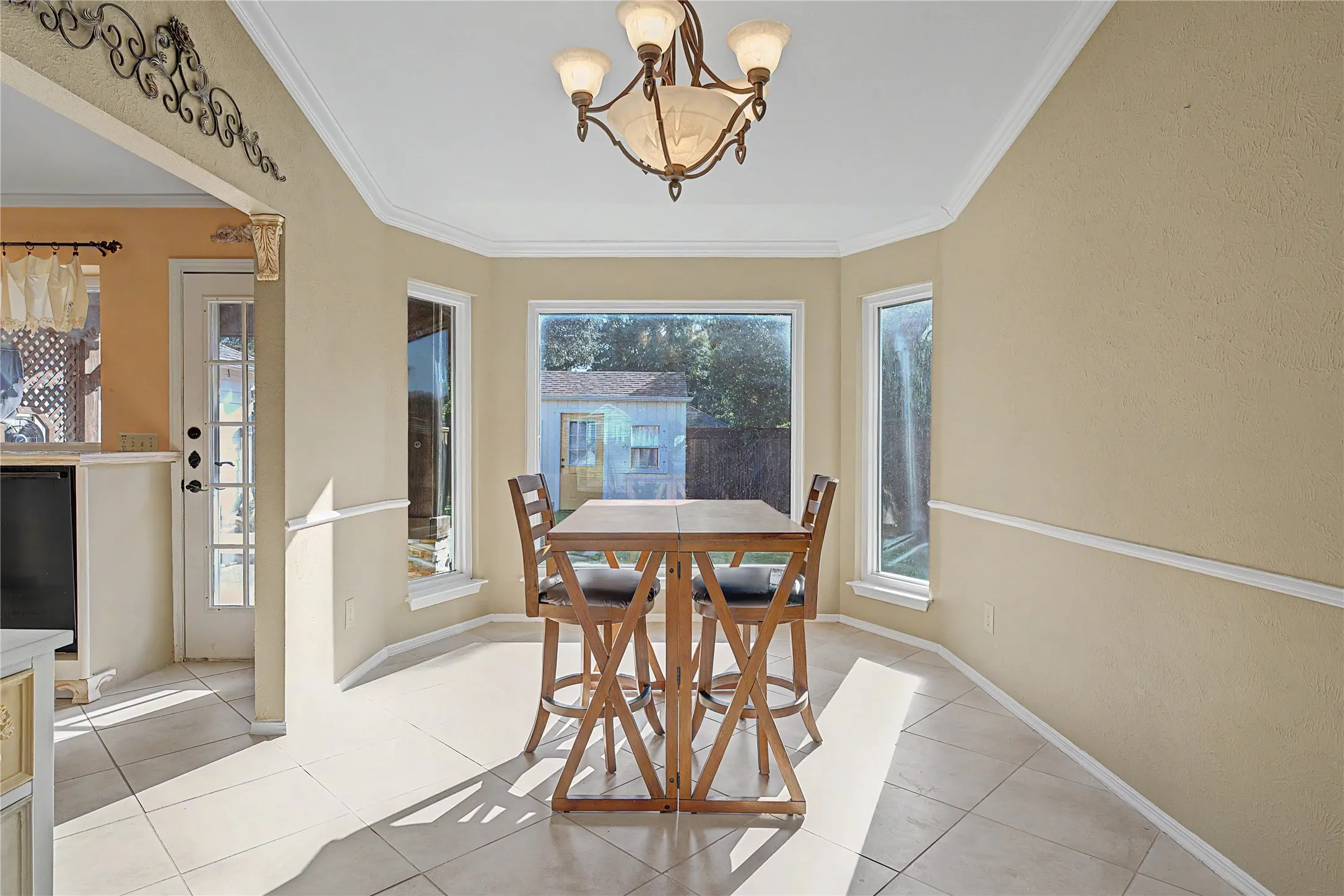 Bay window with three large windows, crown molding, chair rail molding, tiled flooring, and an ornamental light fixture