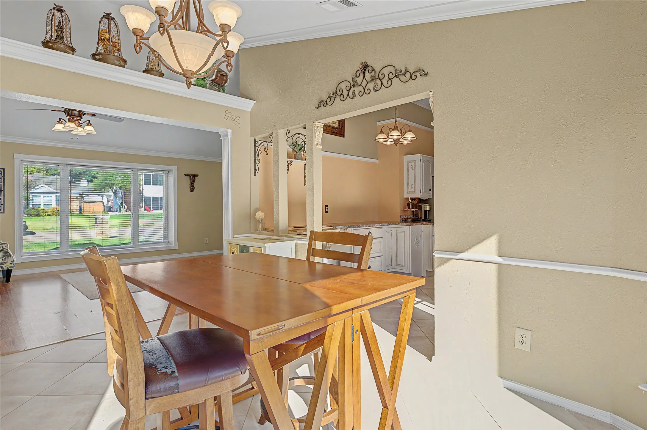 Vaulted ceiling with decorative chandelier, tile flooring, crown molding, and an open doorway to an adjacent room with large picture windows