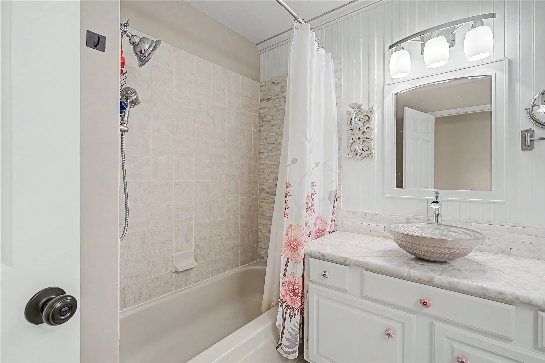 Full bathroom featuring a tub-shower combination with tiled surround, a vanity with a vessel sink, a stone-finish countertop, and beadboard wall paneling
