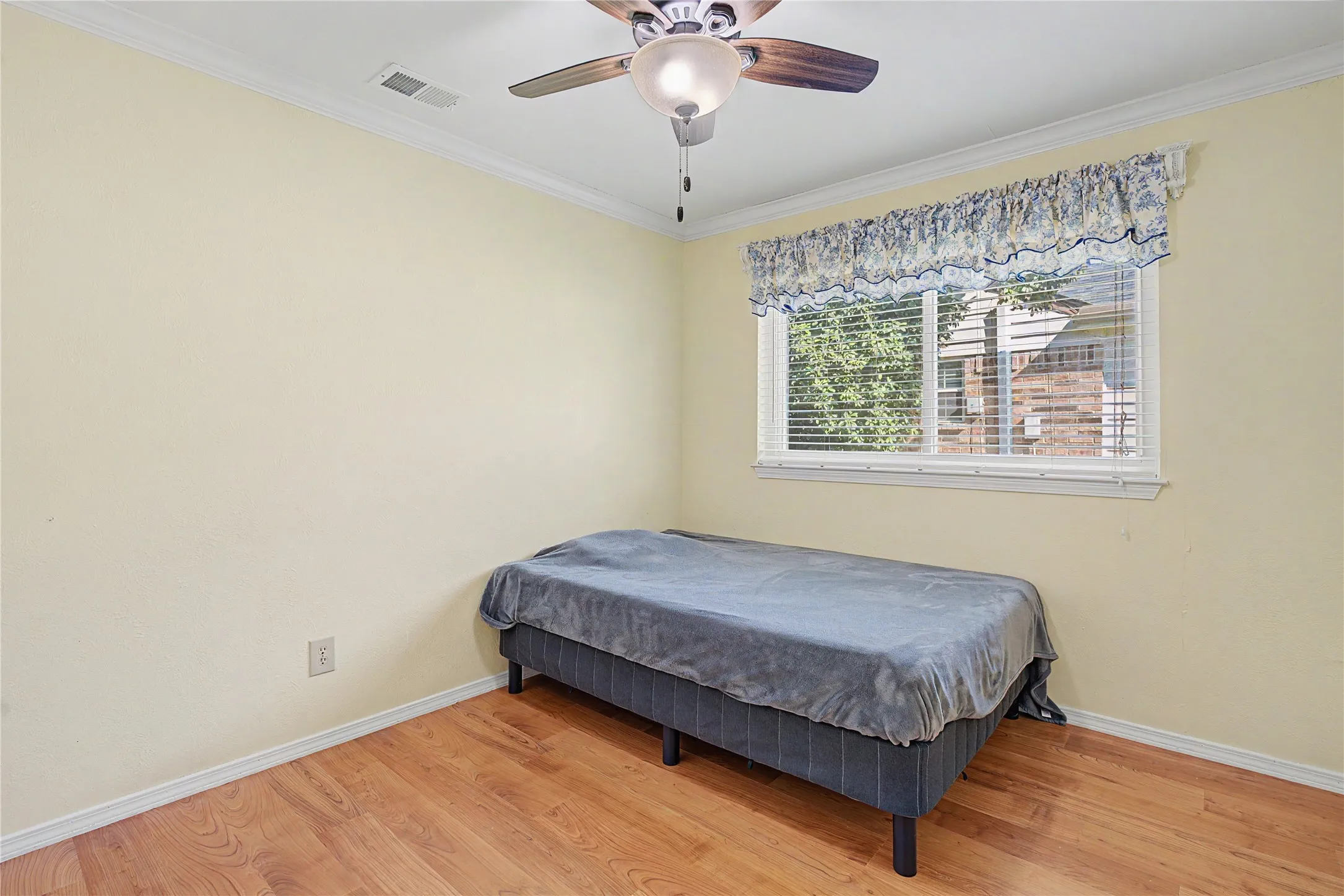 Wood-finish flooring, single window with blinds, ceiling fan with integrated lighting, and crown molding