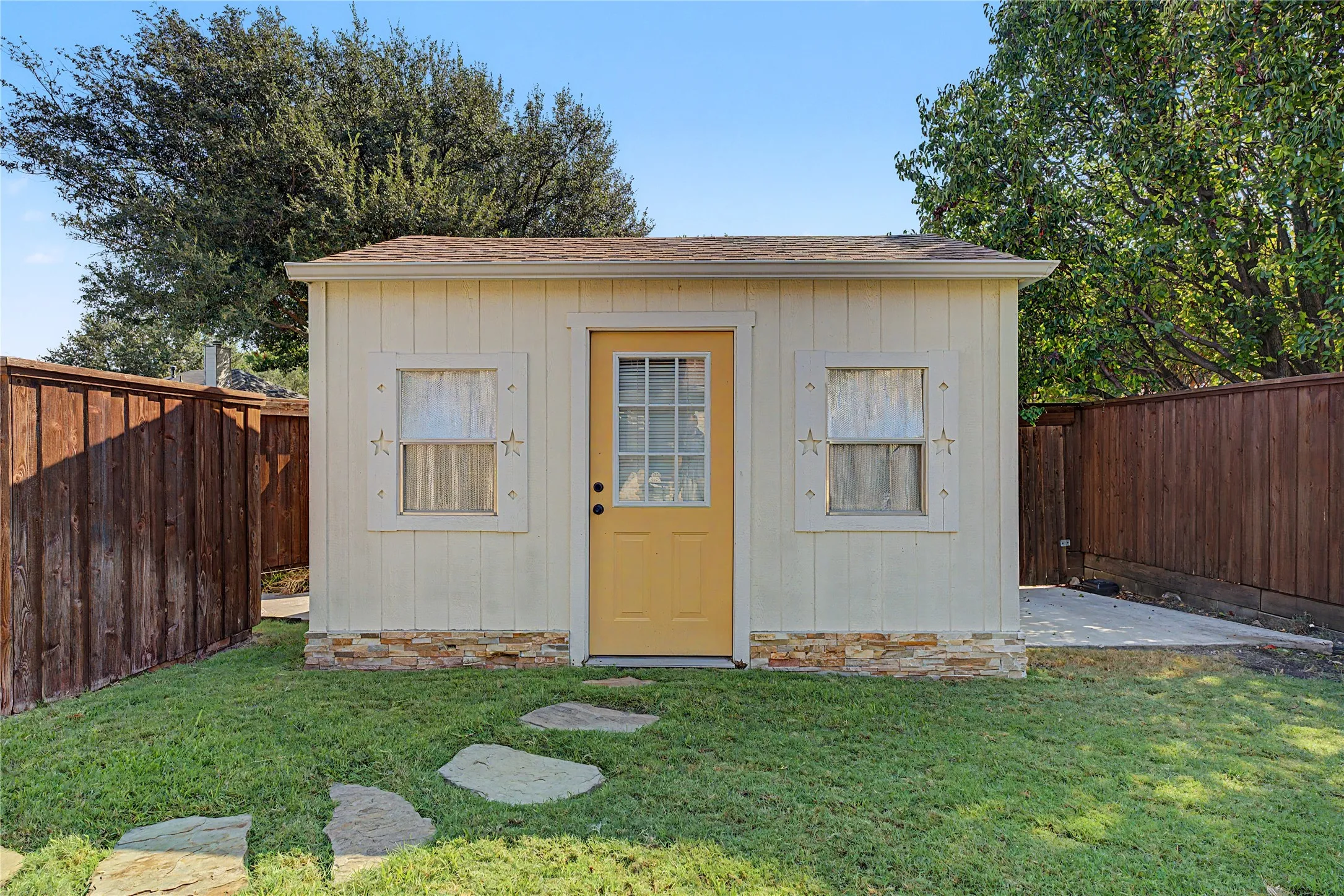 Detached auxiliary building with vertical siding, decorative window trim, a paneled door with glass inserts, and a stone veneer foundation accent