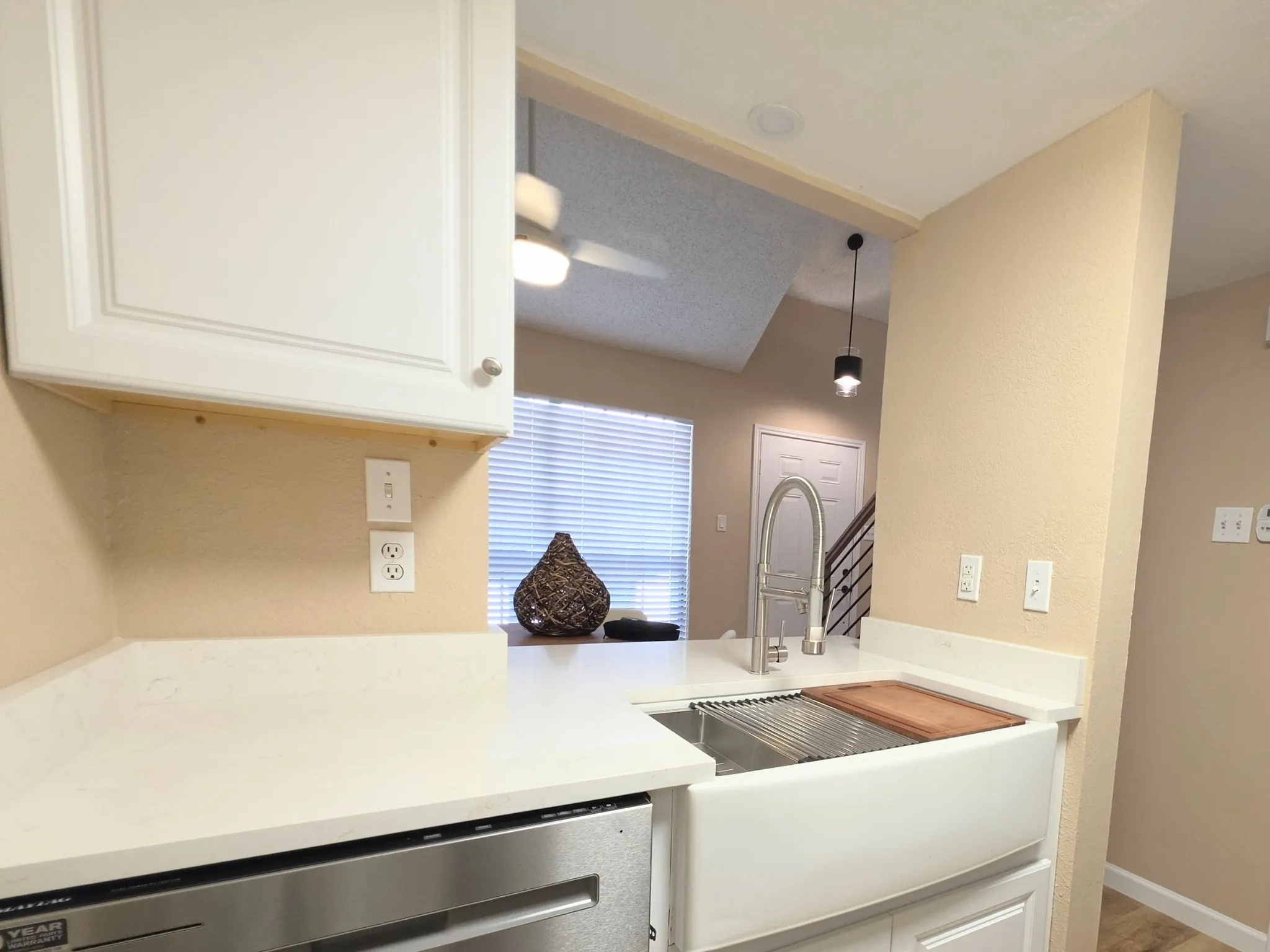 Kitchen featuring a white farmhouse sink, white countertops, stainless steel dishwasher, and white cabinetry
