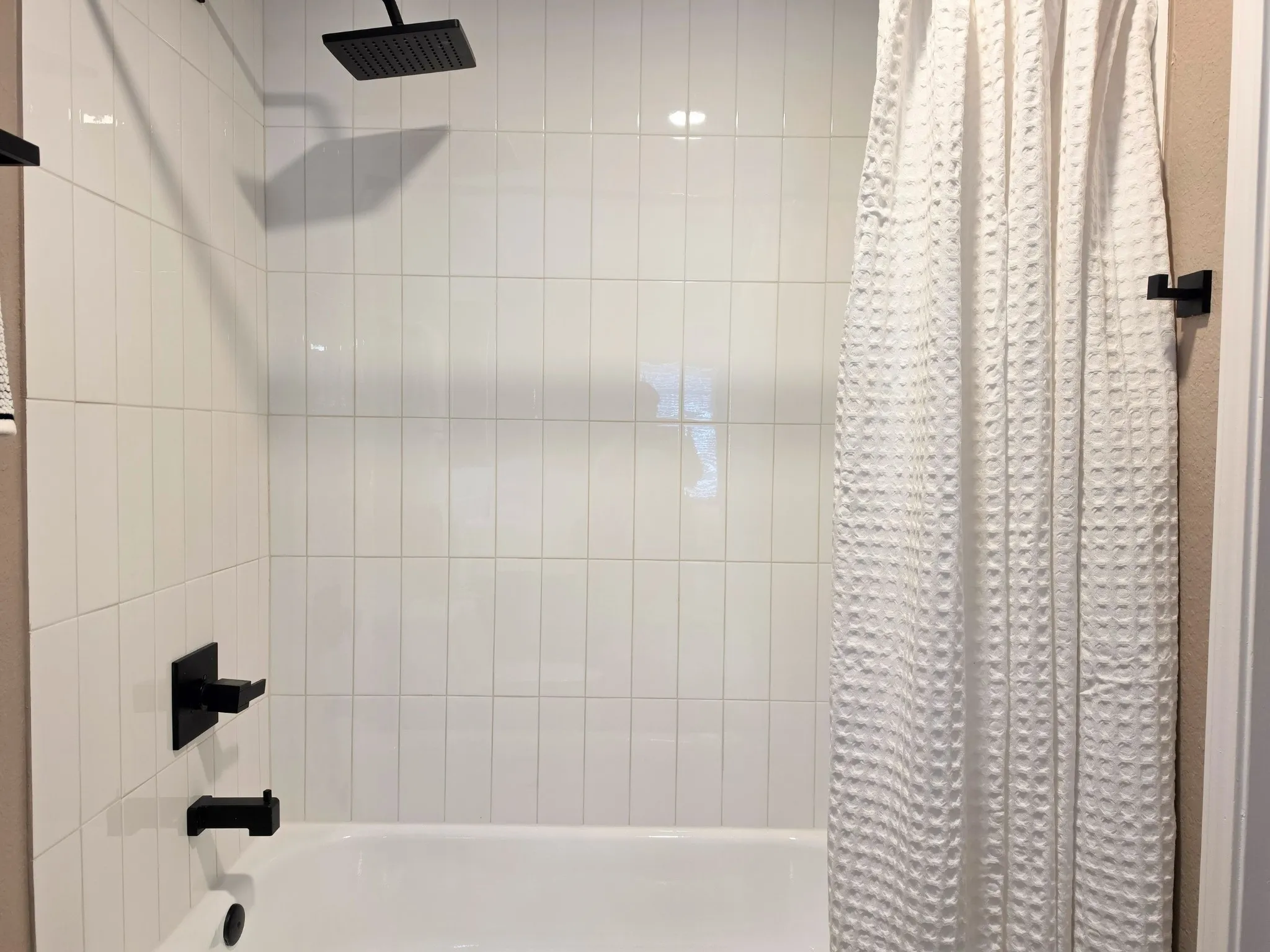 Bathtub and shower combination featuring white vertical subway tile, a square rain showerhead, and matte black fixtures