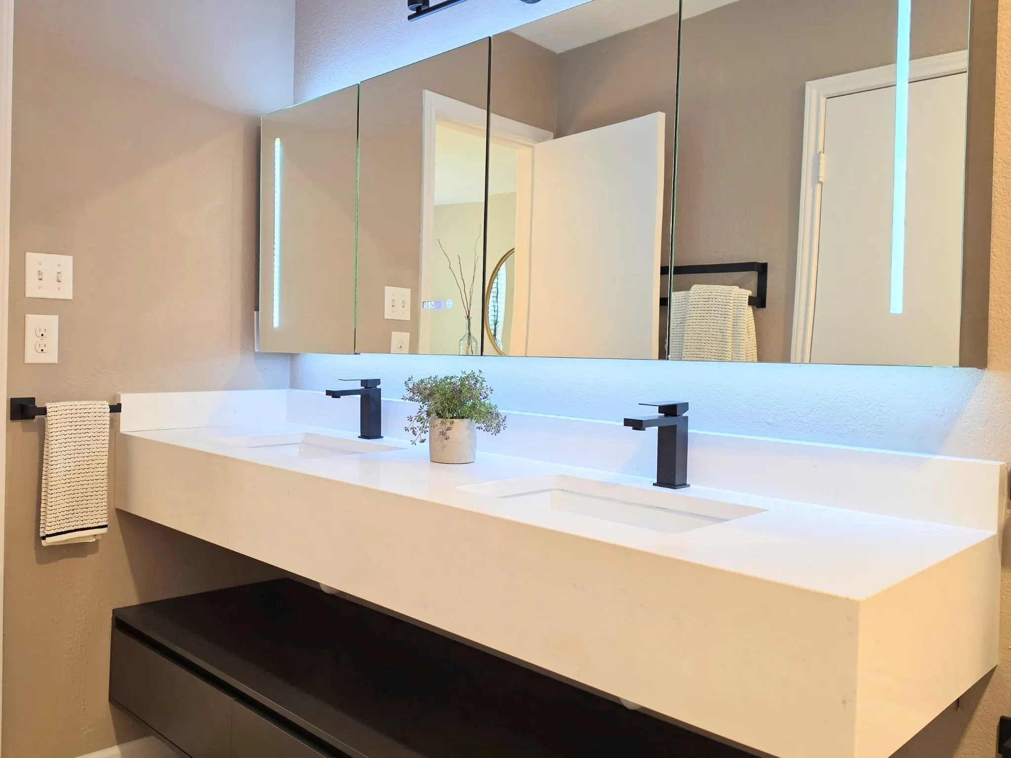 Double vanity with integrated sinks, floating black cabinetry, matte black fixtures, and illuminated fog free​​‌​​​​‌​​‌‌​‌‌​​​‌‌​‌​‌​‌​​​‌​​ mirror