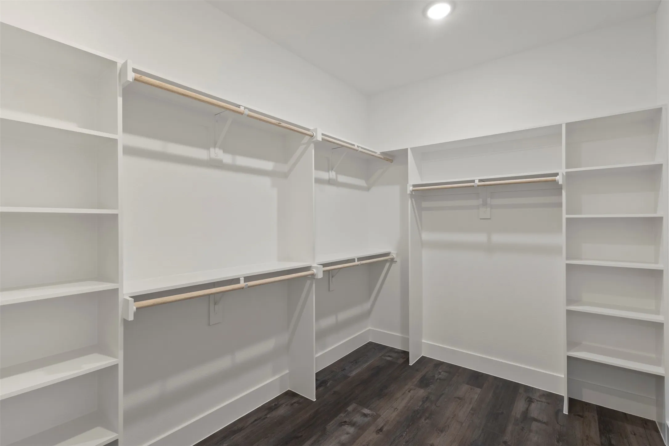 Walk-in closet featuring extensive built-in shelving, multiple hanging rods, dark wood-finish flooring, and recessed ceiling lighting