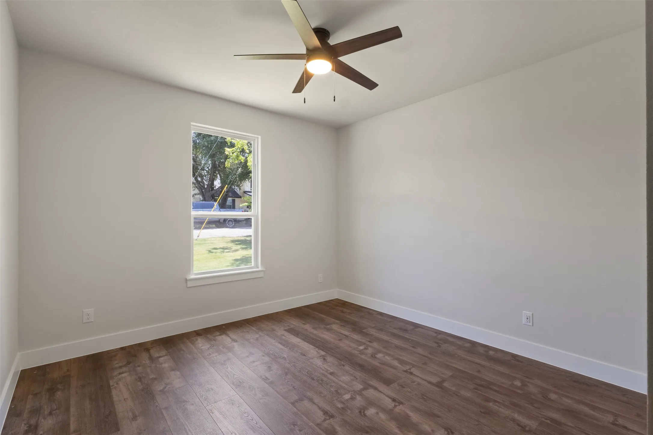 Bright room featuring wood-finish flooring, white baseboards, a single window, and a ceiling fan with integrated lighting
