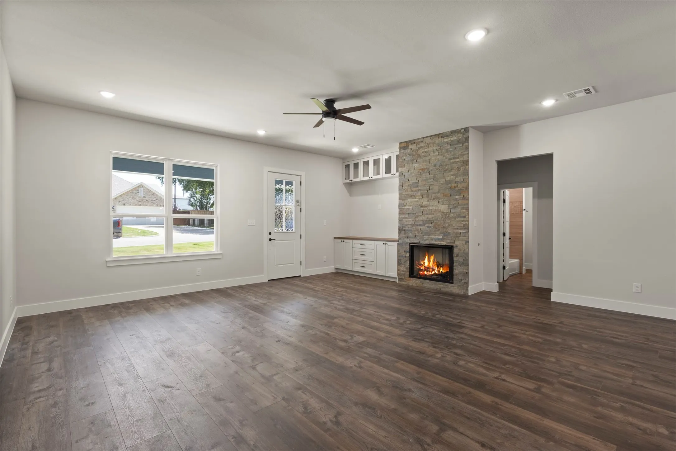 Spacious living area featuring wood-finish flooring, a stone-clad fireplace with an integrated hearth, and recessed lighting