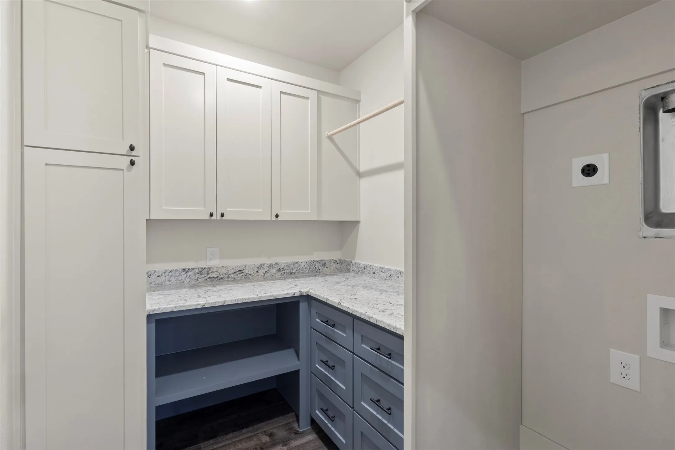 Laundry room featuring light shaker-style cabinetry, a contrasting blue-grey lower cabinet and drawer set, a speckled countertop, and wood-finish flooring