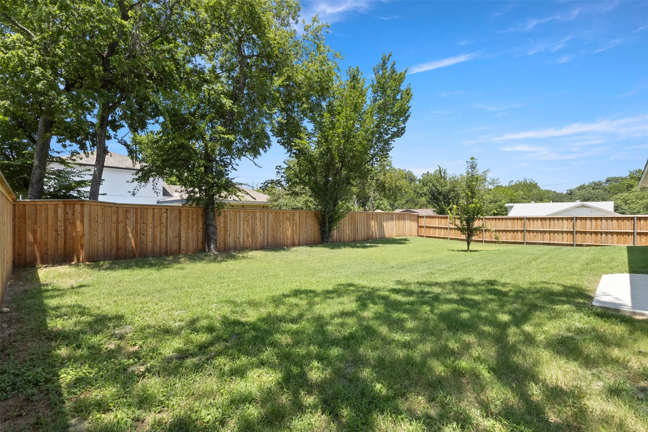 Expansive backyard featuring a new wood privacy fence, mature shade trees, and a concrete patio pad