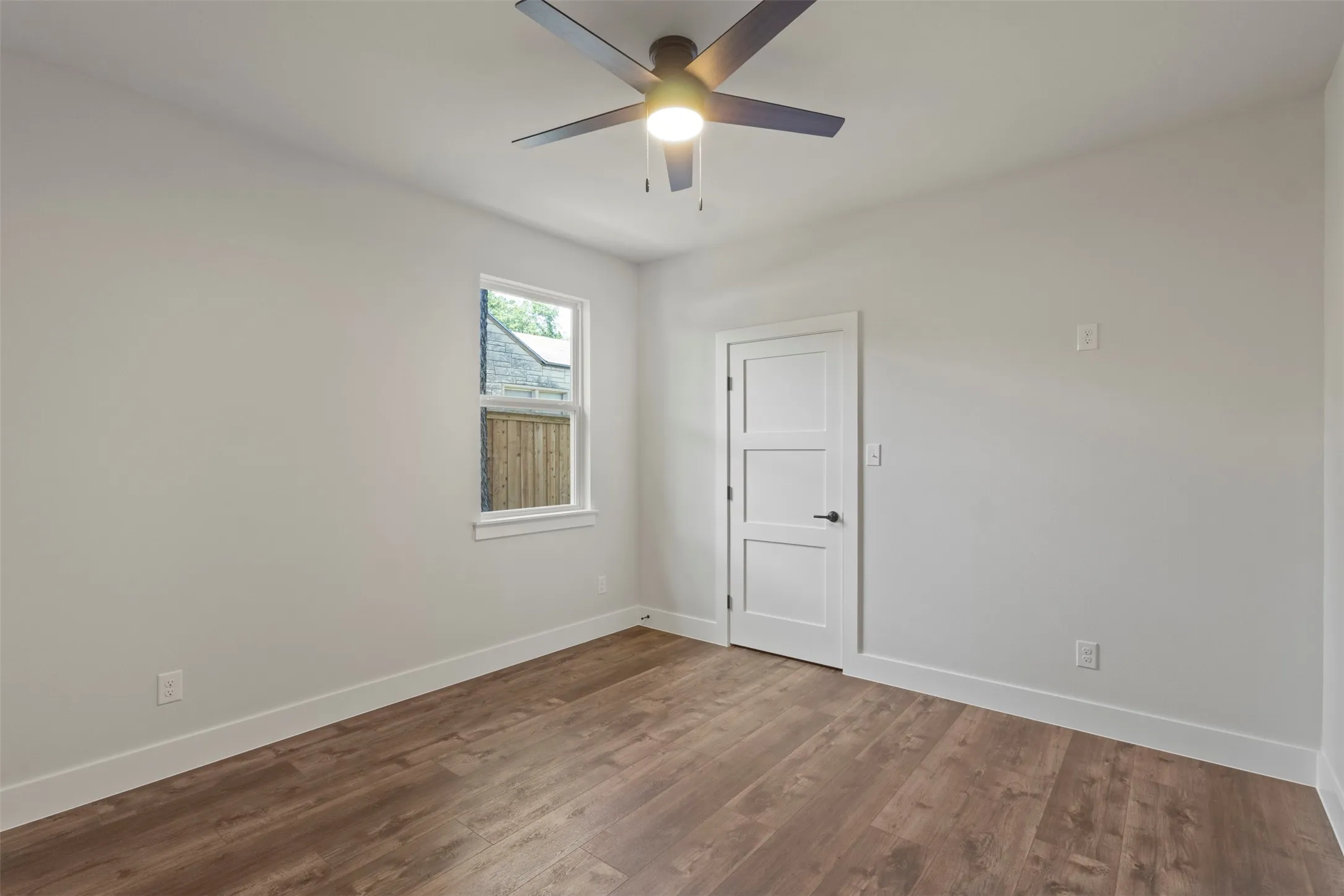 Spacious room featuring wood-finish flooring, a contemporary ceiling fan with integrated lighting, and a white three-panel interior door