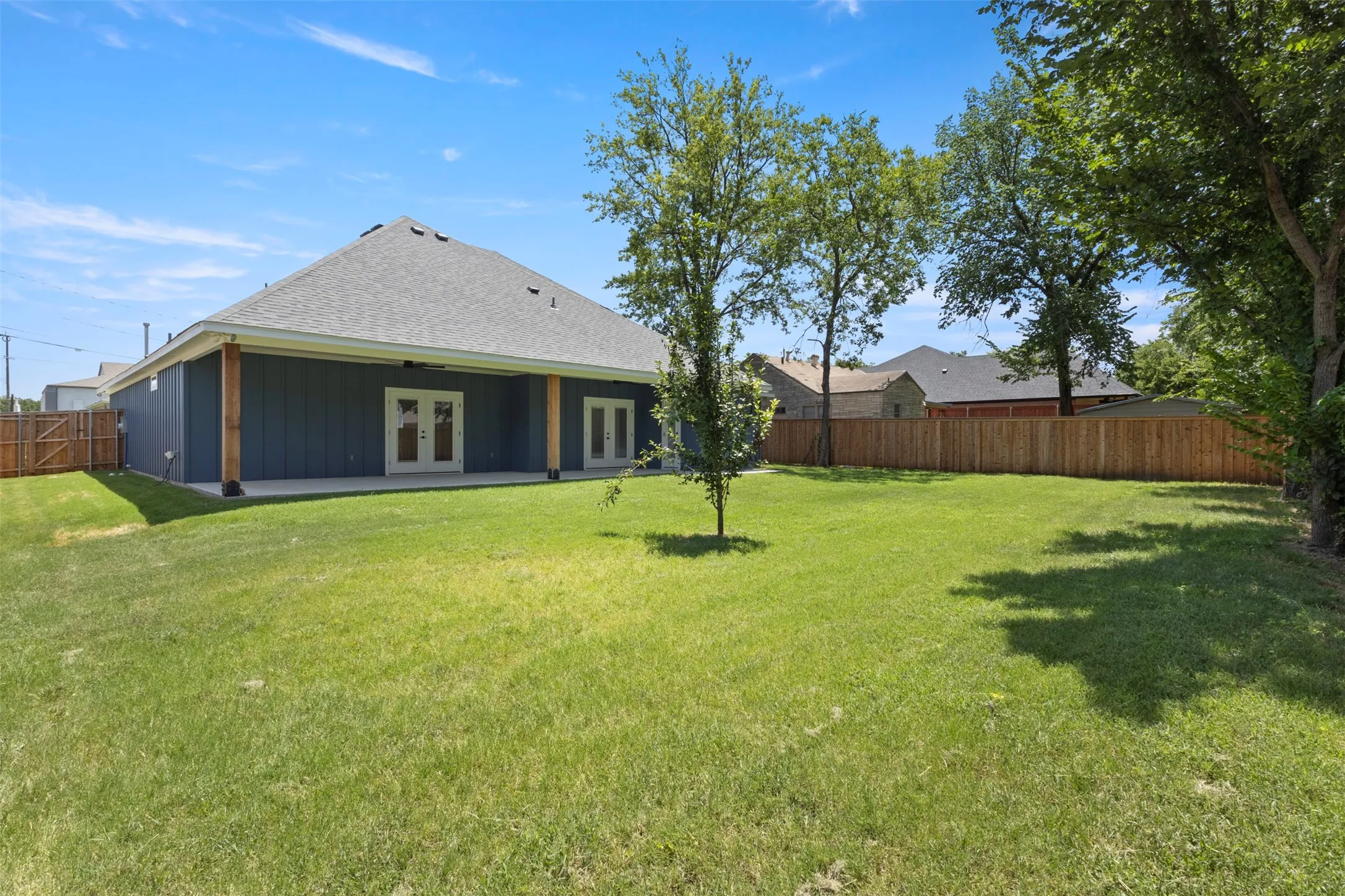Expansive backyard featuring a manicured lawn, full privacy fencing, and mature trees