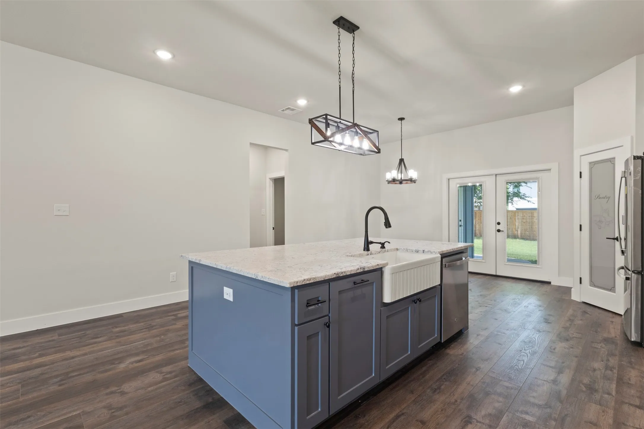 Kitchen featuring a central island with a farmhouse sink, granite countertop, and dark cabinetry