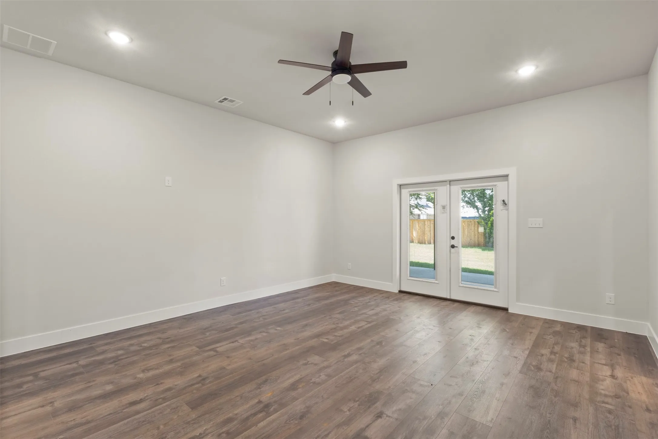 Spacious room featuring wood-finish flooring, white baseboards, and neutral wall paint