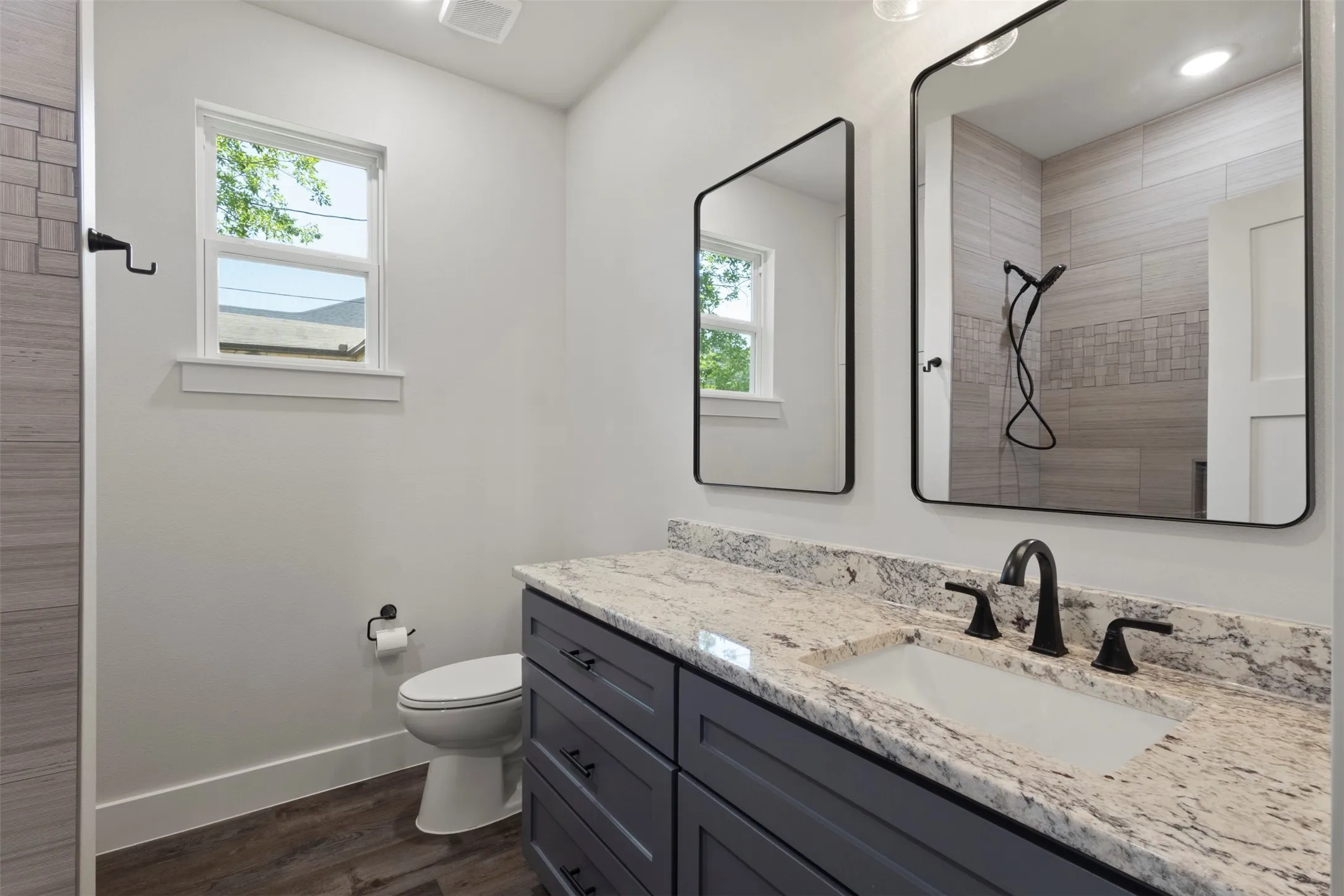 Bathroom featuring a dual-sink vanity with granite countertop, matte black fixtures, and wood-finish flooring