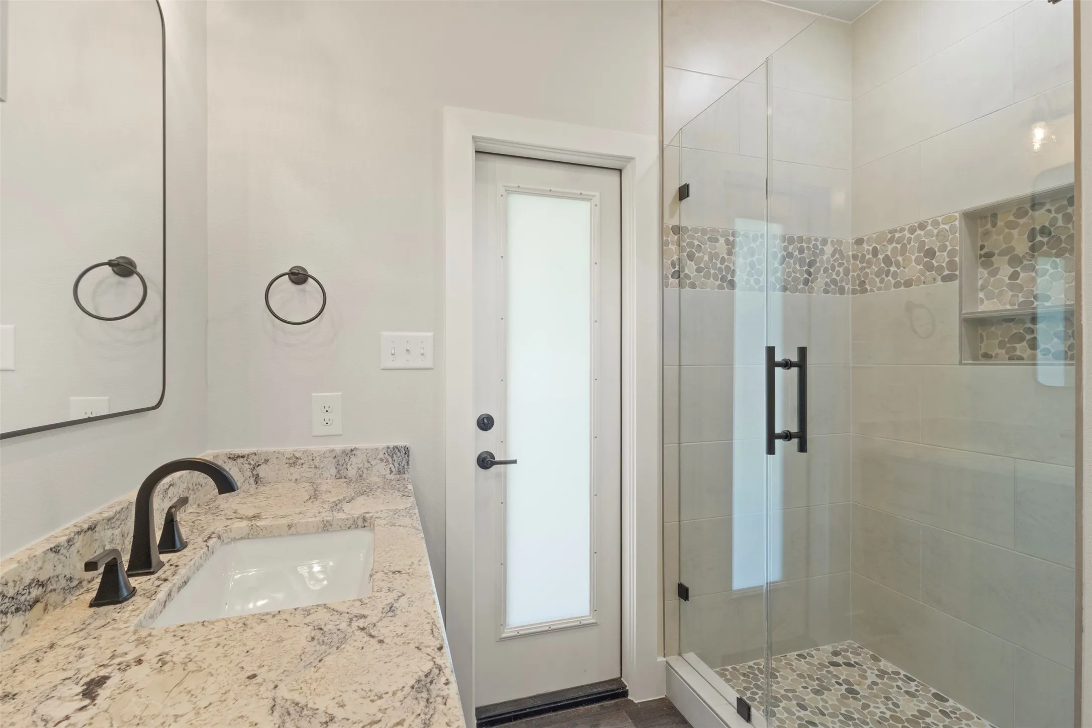 Bathroom featuring a walk-in shower with a frameless glass enclosure, pebble tile accents, and built-in shelving