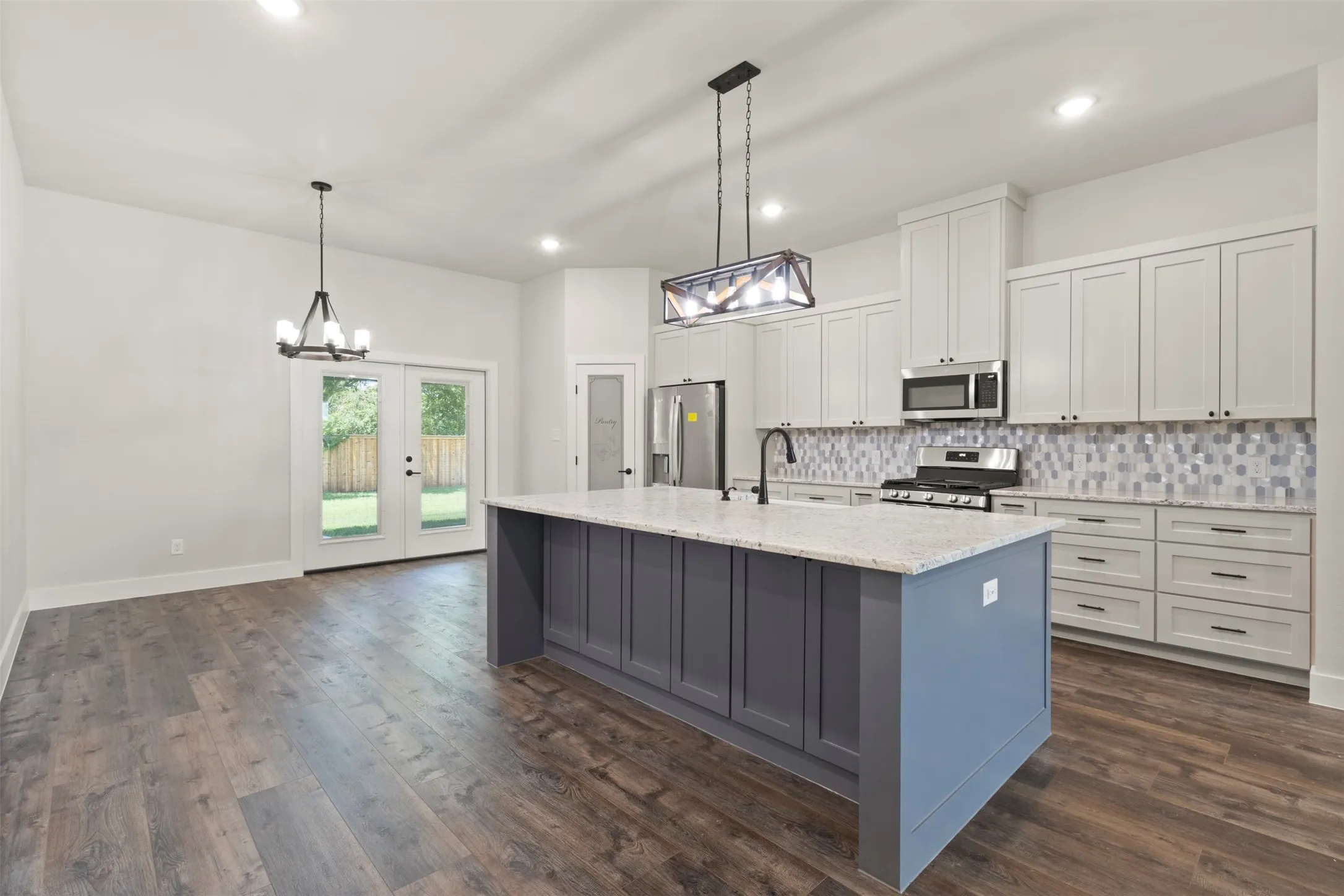 Spacious kitchen featuring a large island with a light-colored countertop, abundant light-toned cabinetry, stainless steel appliances, a decorative tile backsplash, and wood-finish flooring