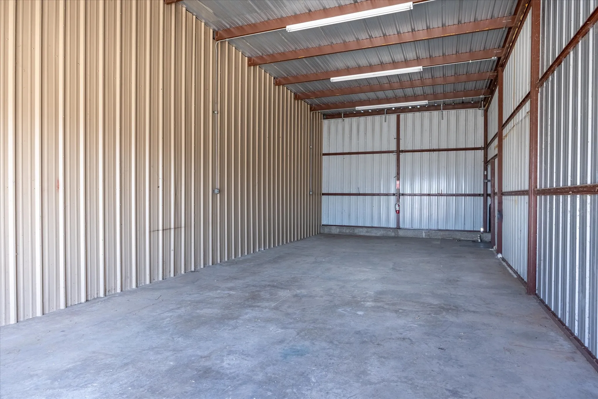 Spacious storage unit featuring corrugated metal walls, a concrete floor, exposed metal framing, and fluorescent lighting fixtures