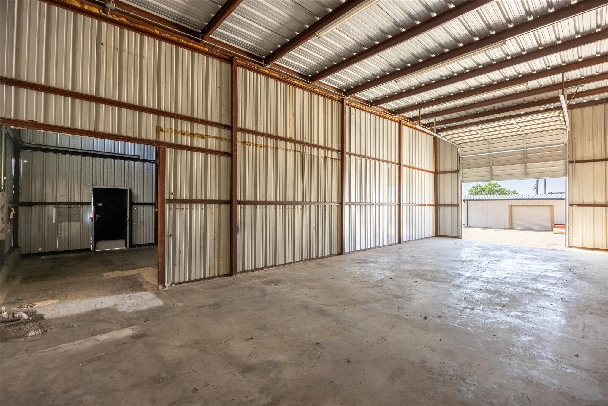 Spacious industrial interior featuring a concrete floor, corrugated metal walls, exposed structural beams, and an overhead door