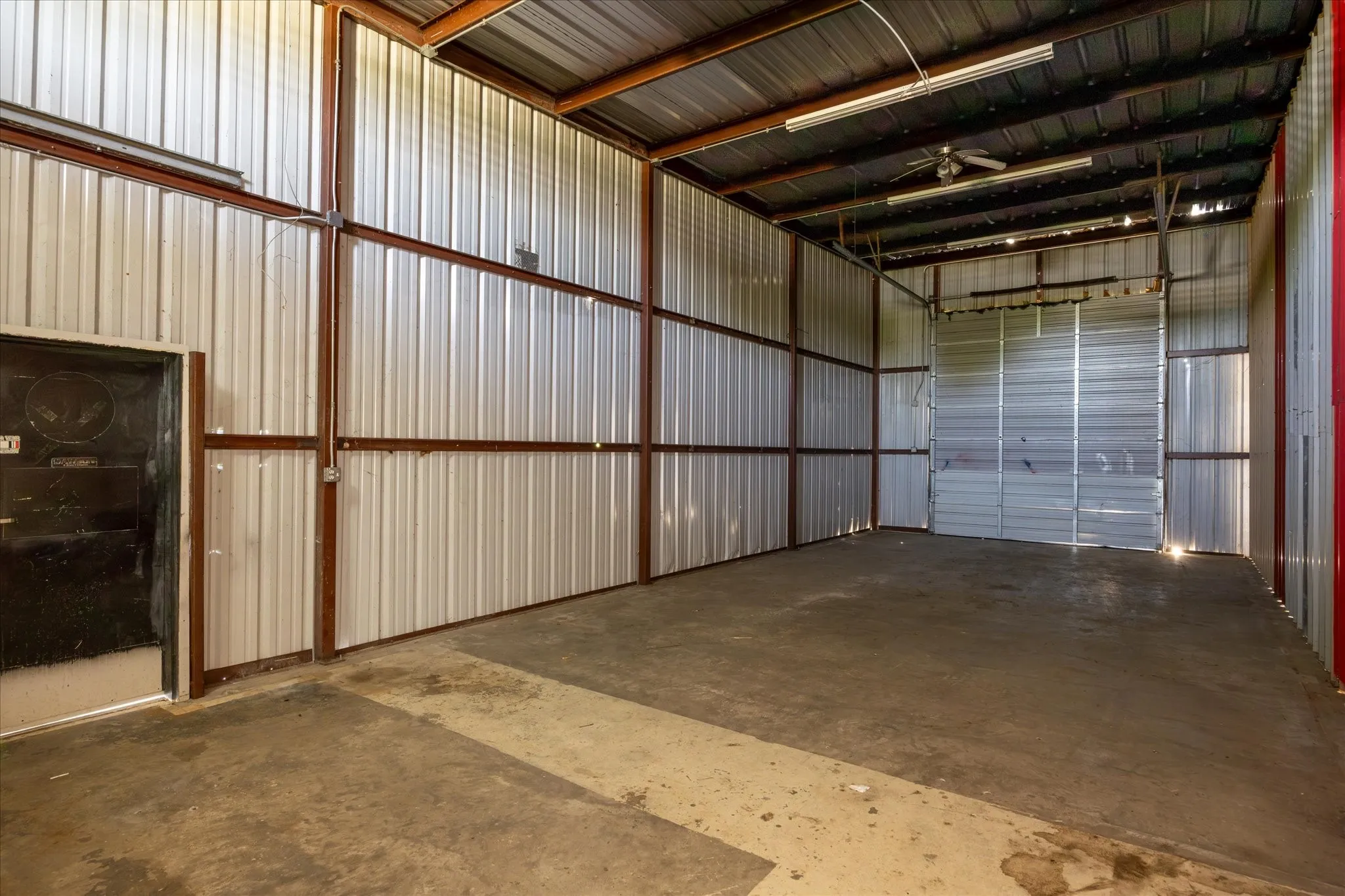 Spacious industrial interior featuring corrugated metal walls with exposed structural beams, a concrete floor, and a large roll-up door