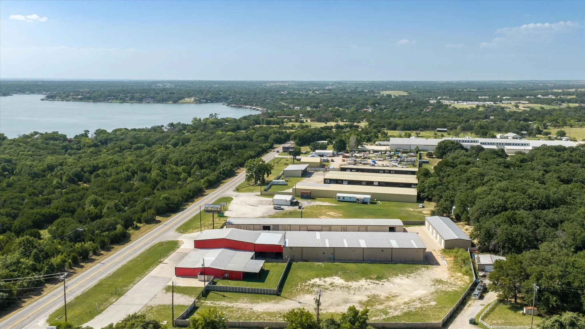 Expansive commercial property featuring multiple buildings, direct road frontage, perimeter fencing, and proximity to a large body of water