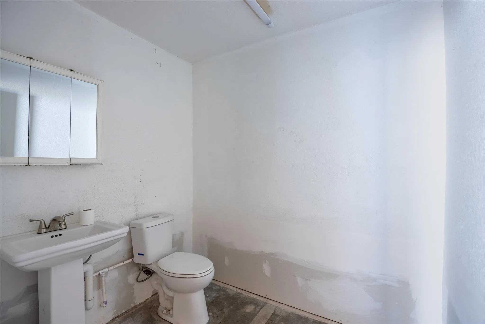 Functional bathroom with a pedestal sink, white toilet, and tri-fold medicine cabinet