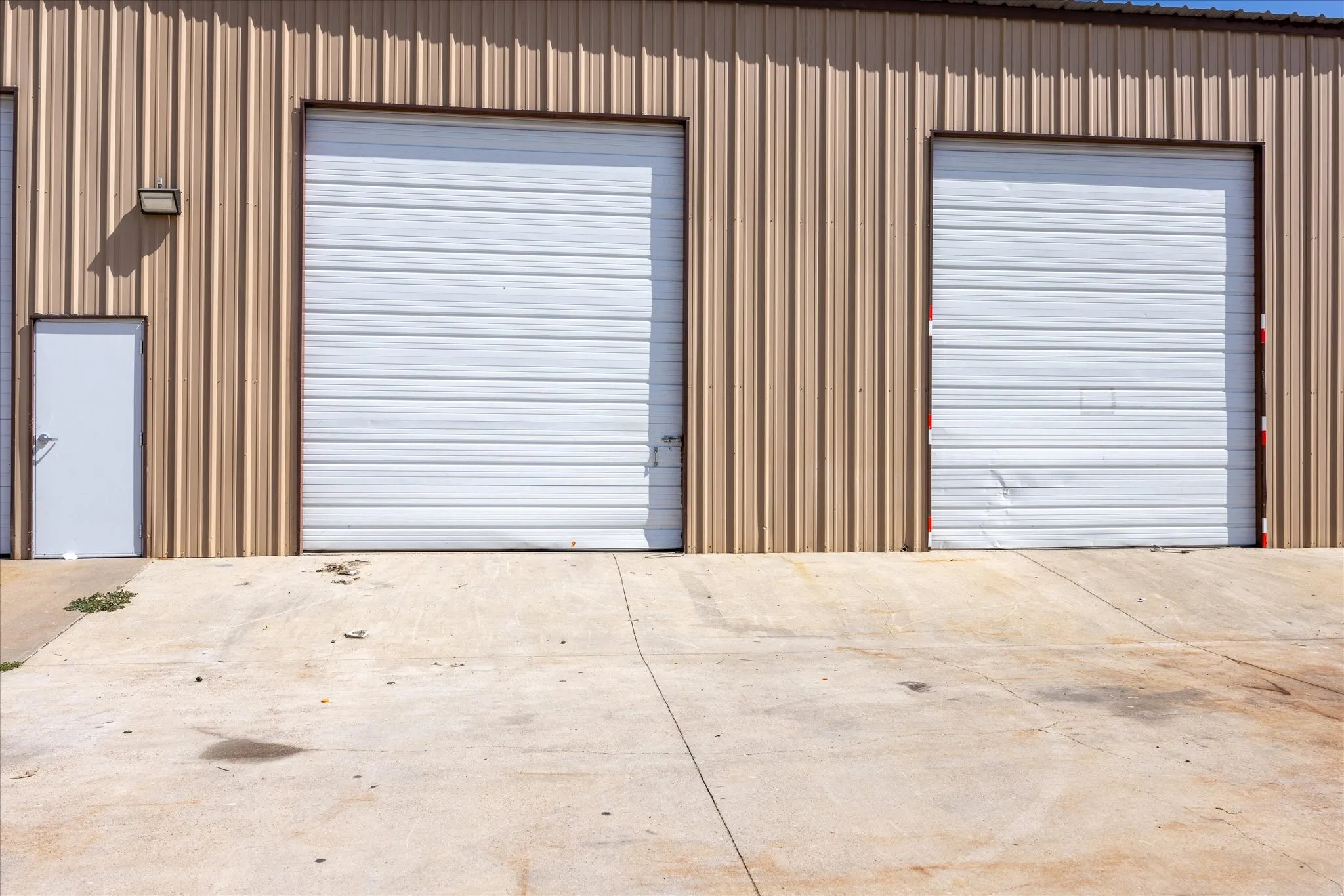 Corrugated metal exterior featuring two roll-up doors, one service door, and a concrete approach