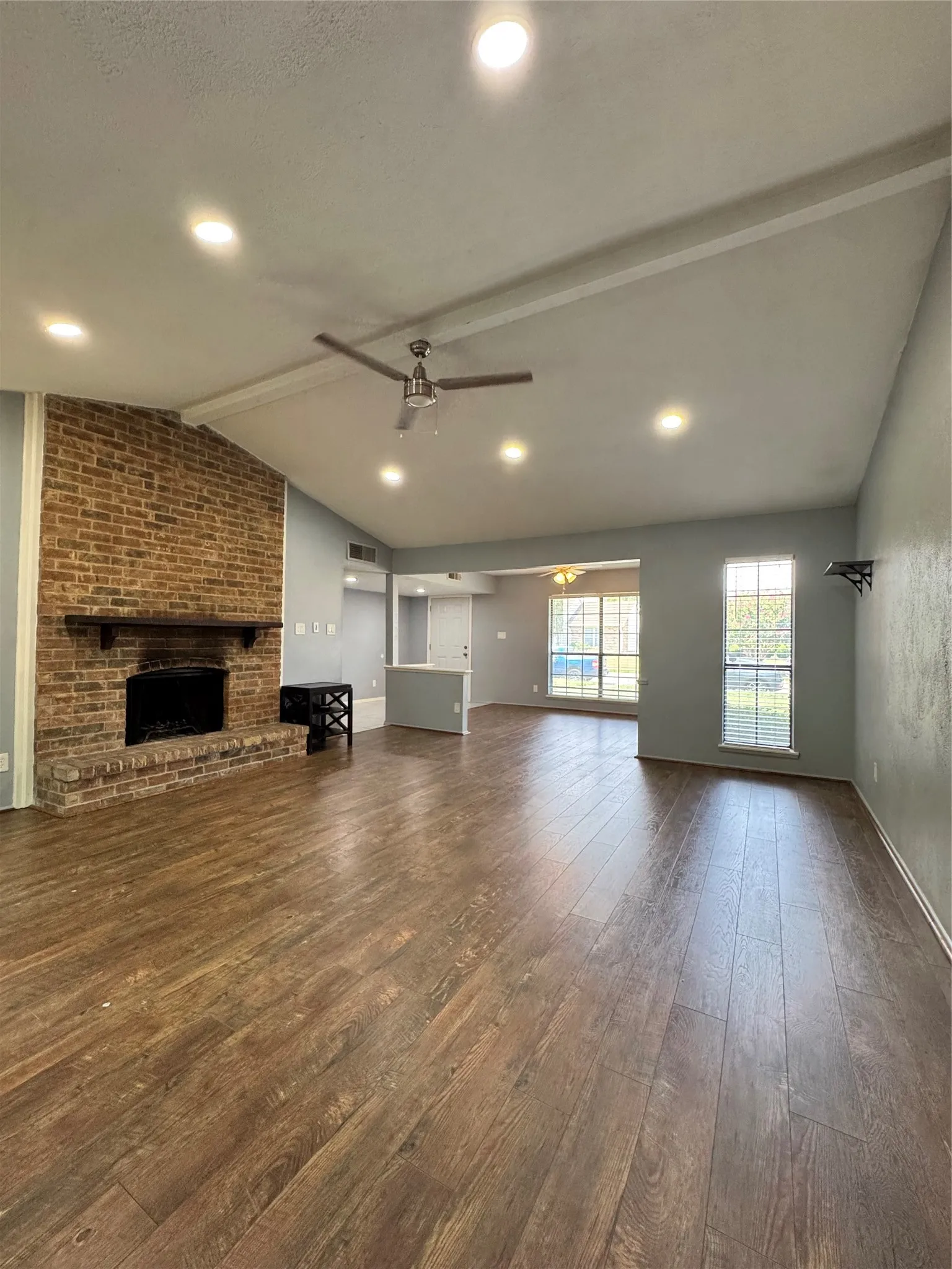 Spacious living area featuring a brick fireplace with a wood mantel, wood-finish flooring, recessed lighting, and a vaulted ceiling with exposed beams
