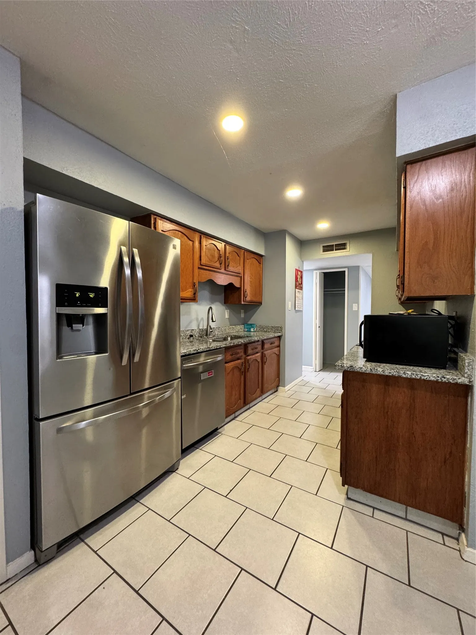 Kitchen featuring stainless steel appliances, wood cabinetry, stone countertops, and recessed lighting