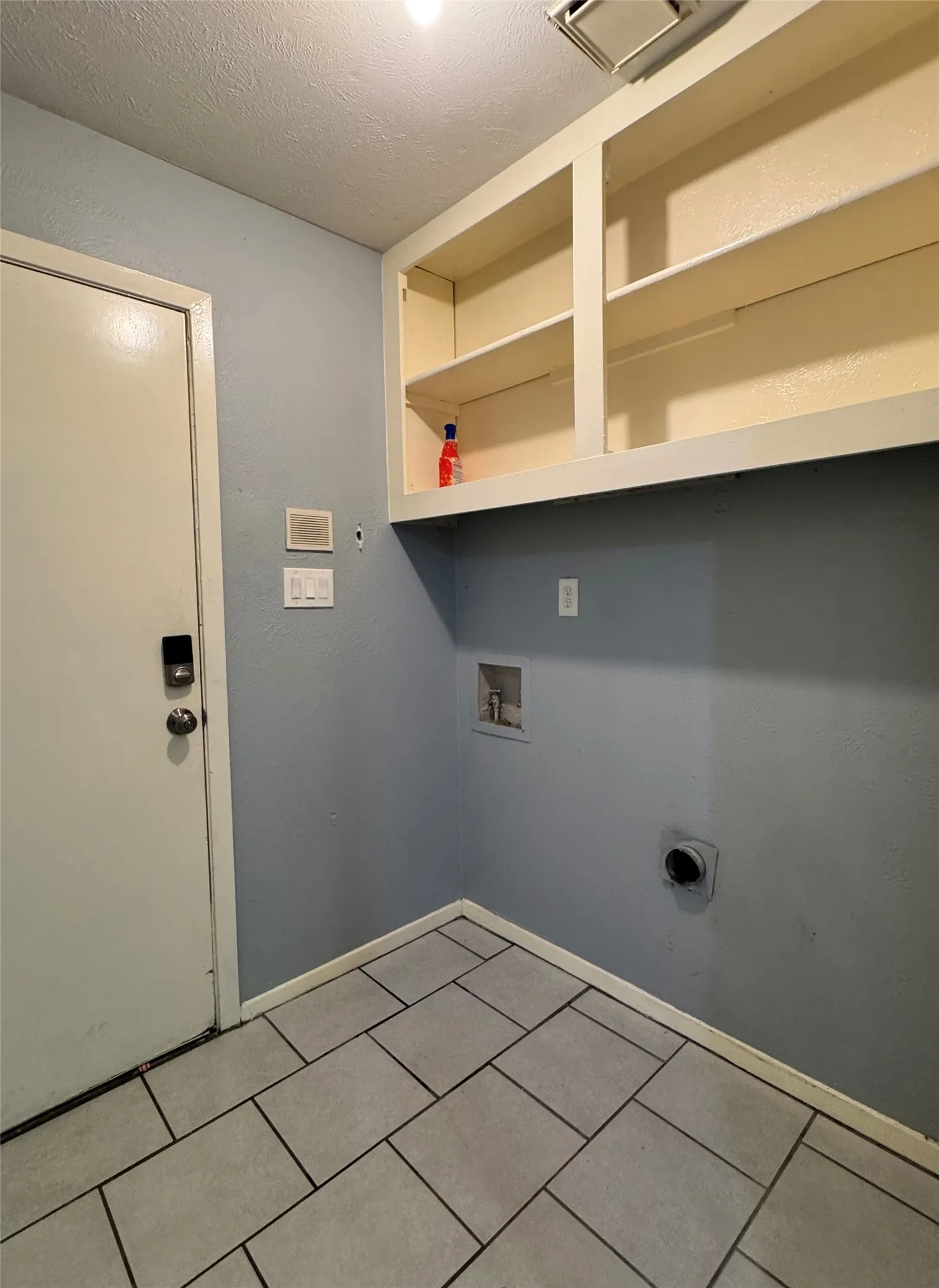 Utility area featuring built-in upper cabinetry, light blue wall paint, and gray rectangular tile flooring