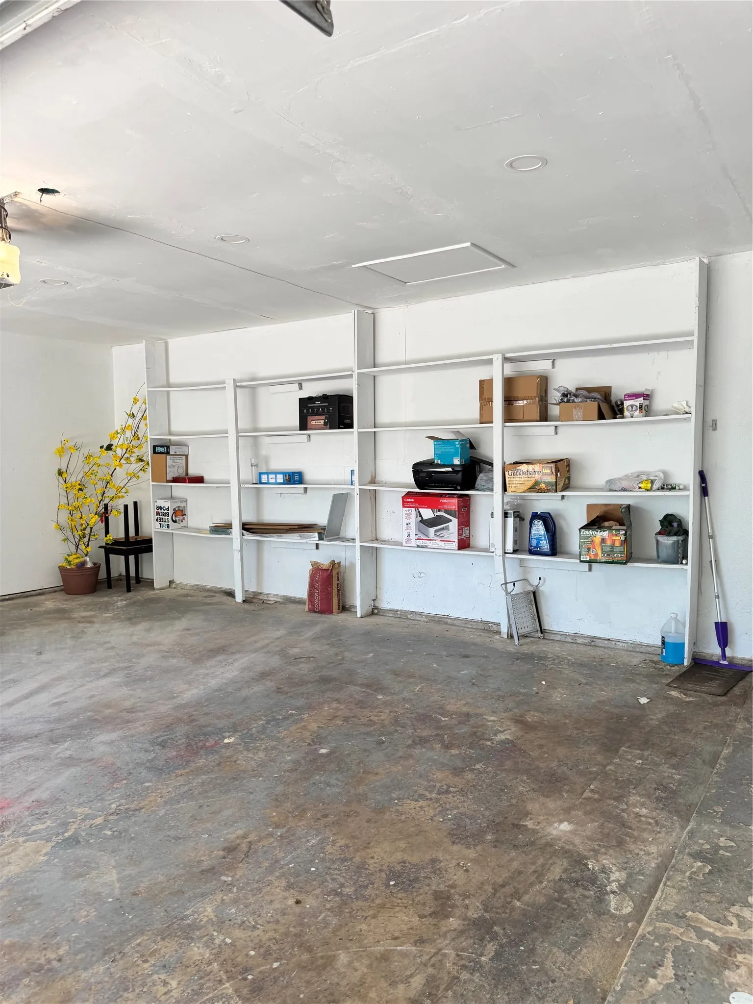 Garage interior featuring built-in shelving, concrete flooring, recessed lighting, and a drop ceiling with an access panel