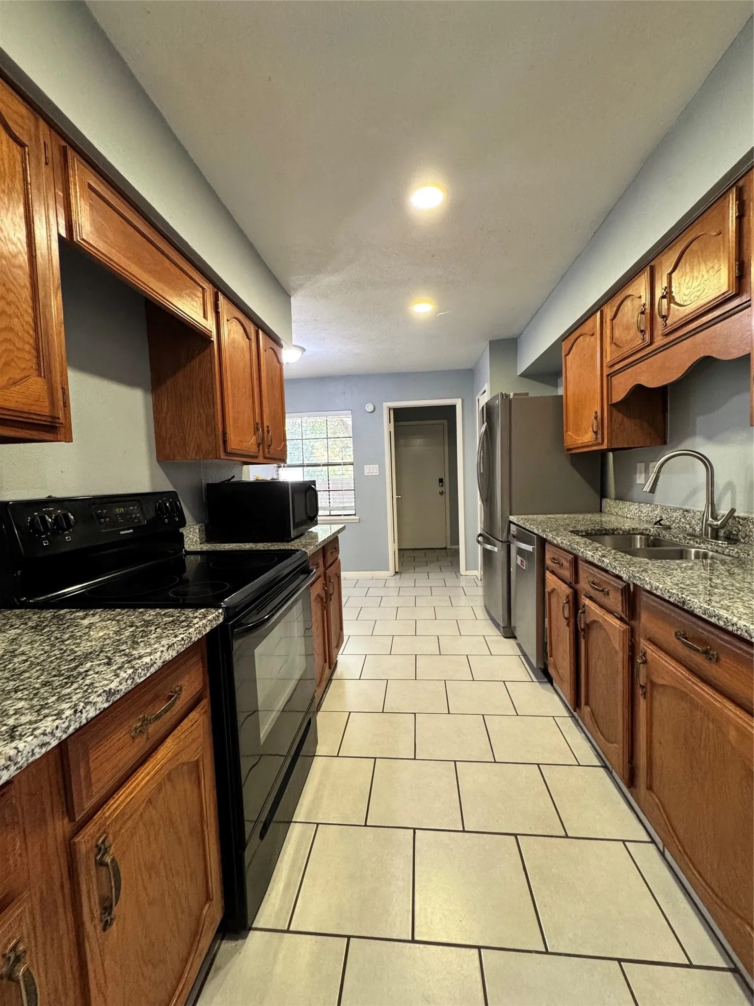 Galley kitchen featuring light-toned tile flooring, wood cabinetry, stone countertops, and recessed lighting