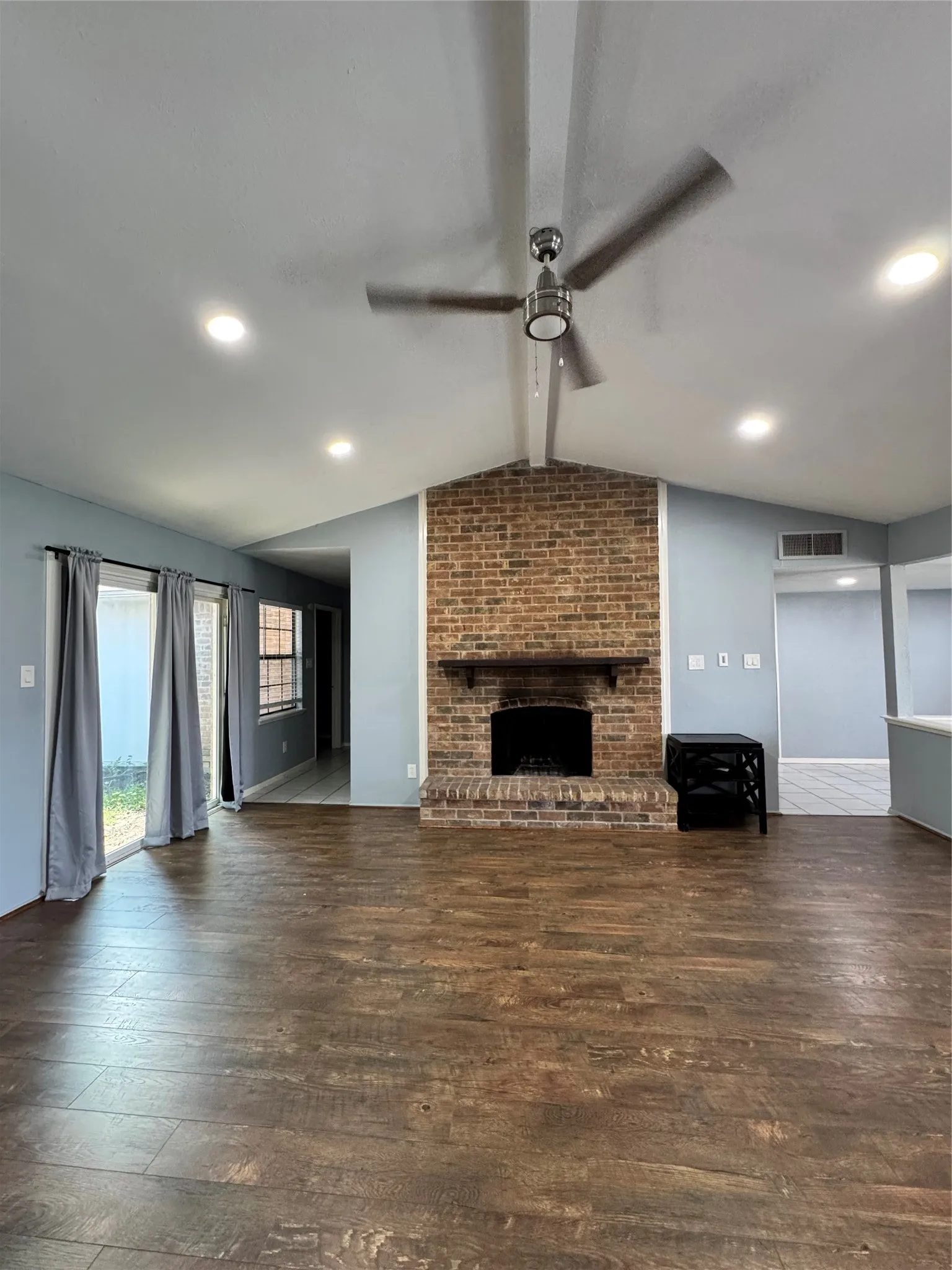 Living area featuring a brick-surround fireplace with a wood mantel, vaulted ceiling with a ceiling fan, recessed lighting, and wood-finish flooring