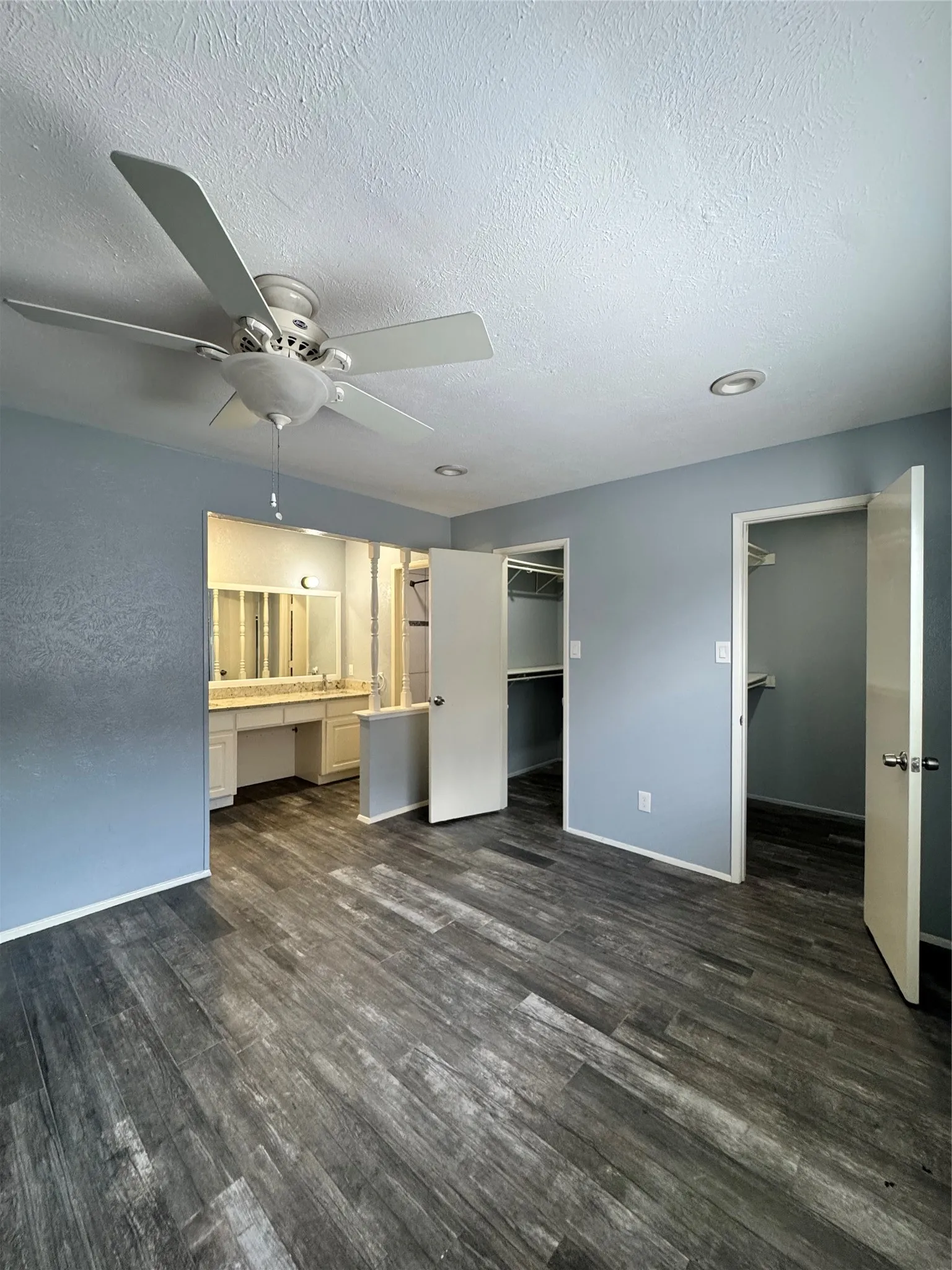 Spacious room featuring wood-finish flooring, light blue walls, and a ceiling fan