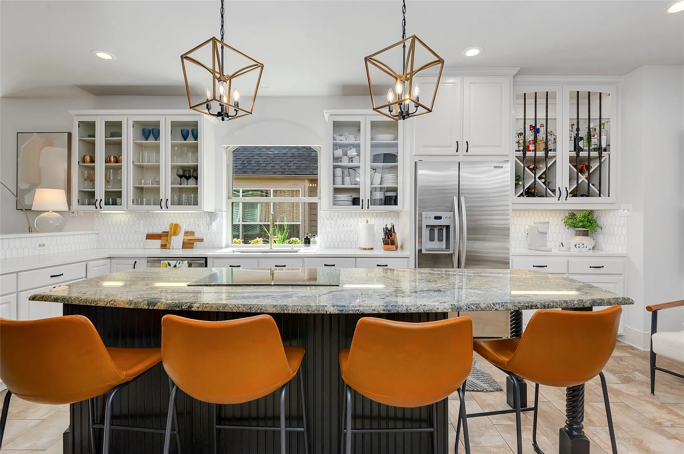 Spacious kitchen featuring a large island with a natural stone countertop, white shaker cabinetry with glass fronts, a stainless steel refrigerator, and built-in wine storage
