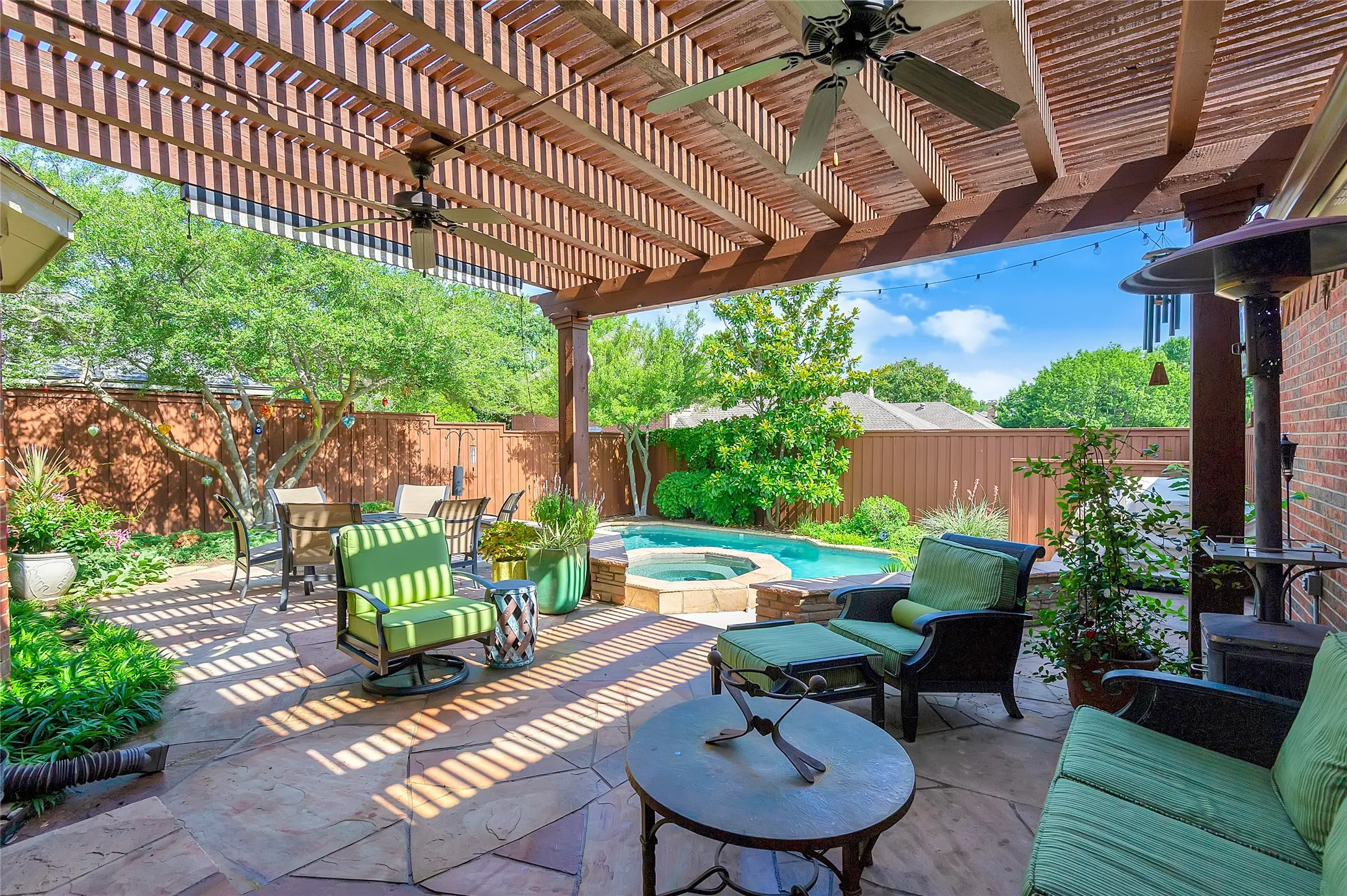 Expansive outdoor living area featuring a wood pergola with ceiling fans, flagstone patio, brick exterior, in-ground pool, and spa