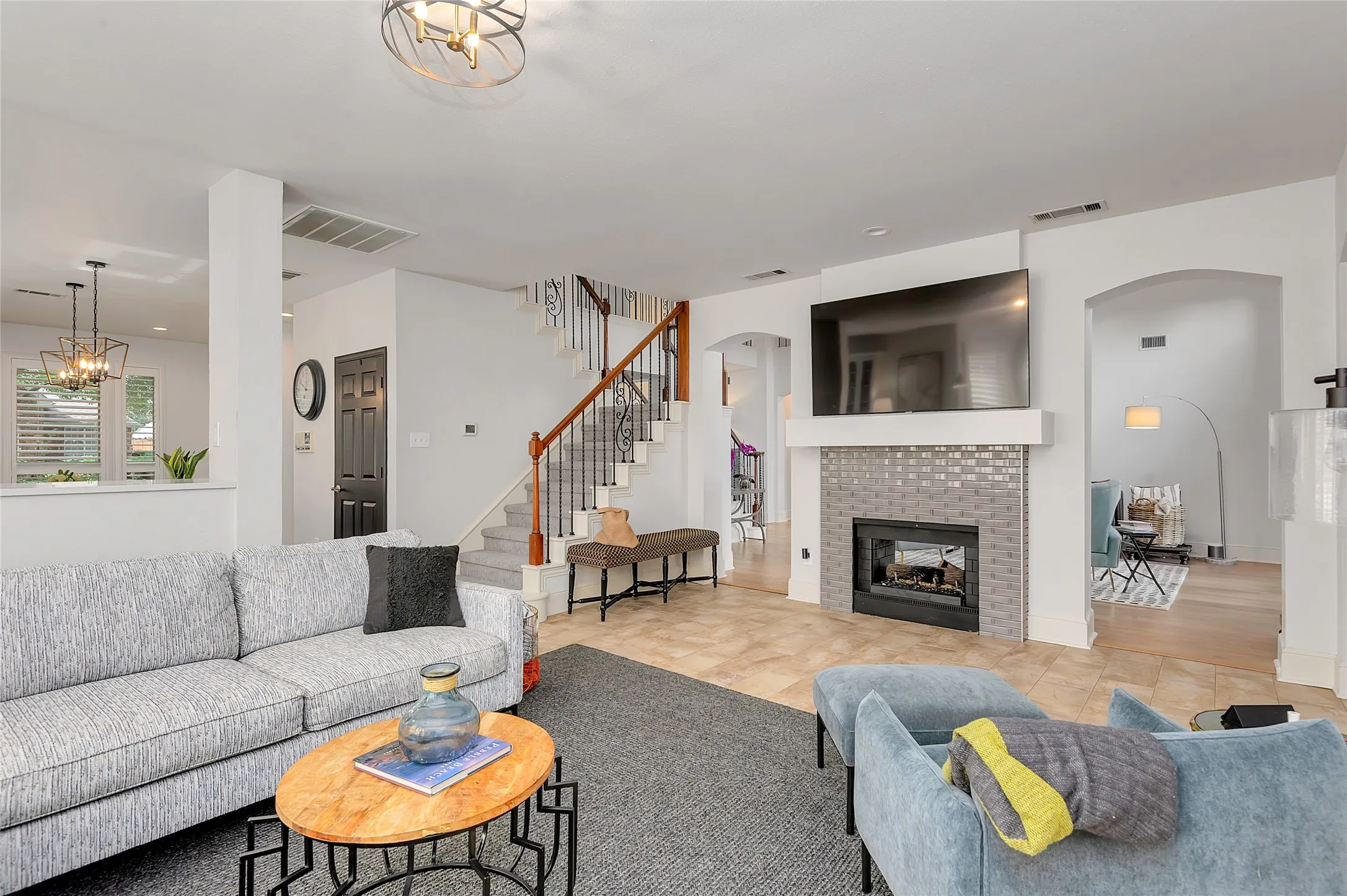 Living area featuring a tiled fireplace with a textured surround, a staircase with wood handrails and iron balusters, and arched doorways